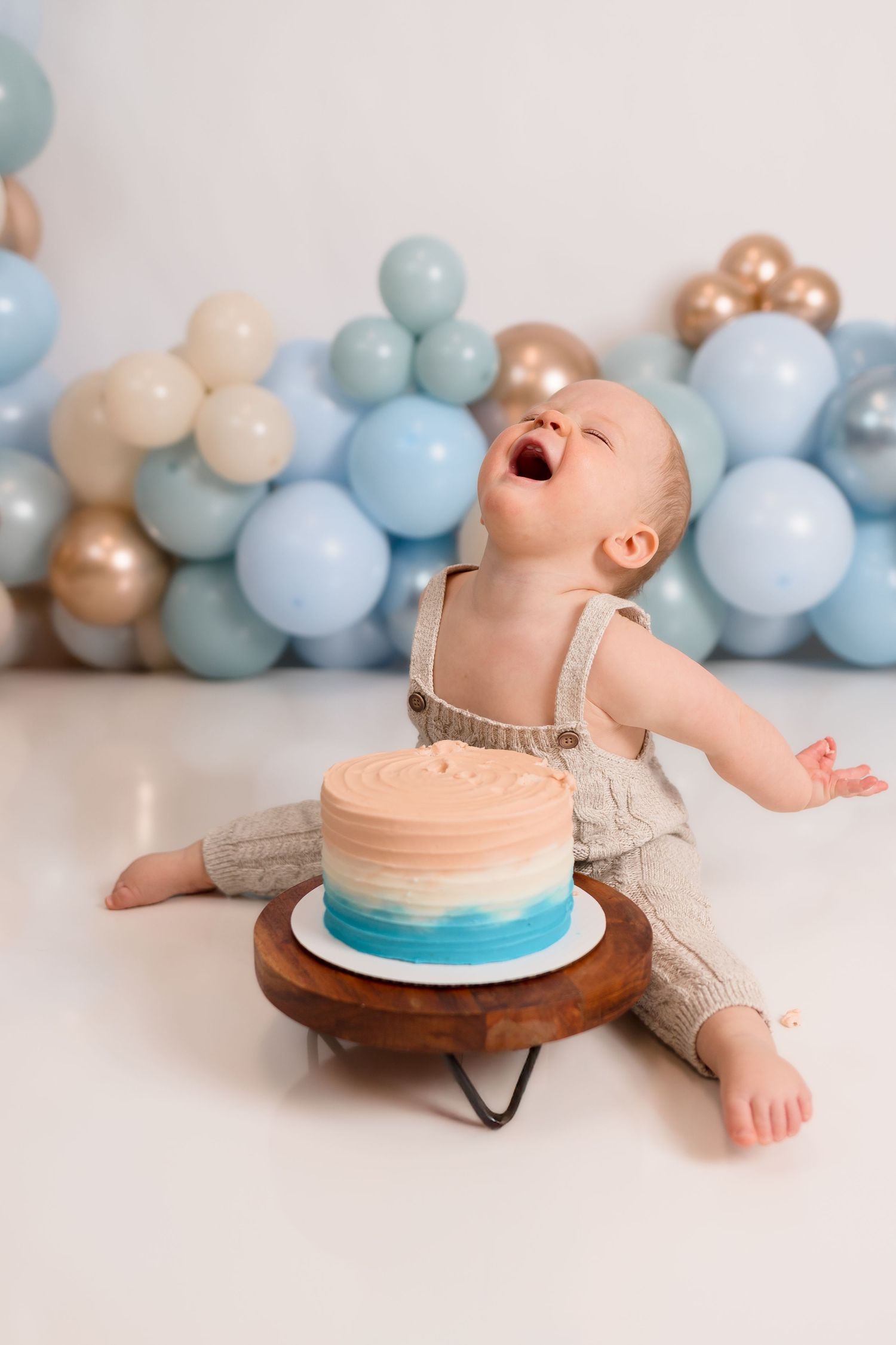 Baby in beige outfit having fun with blue and peach birthday cake.