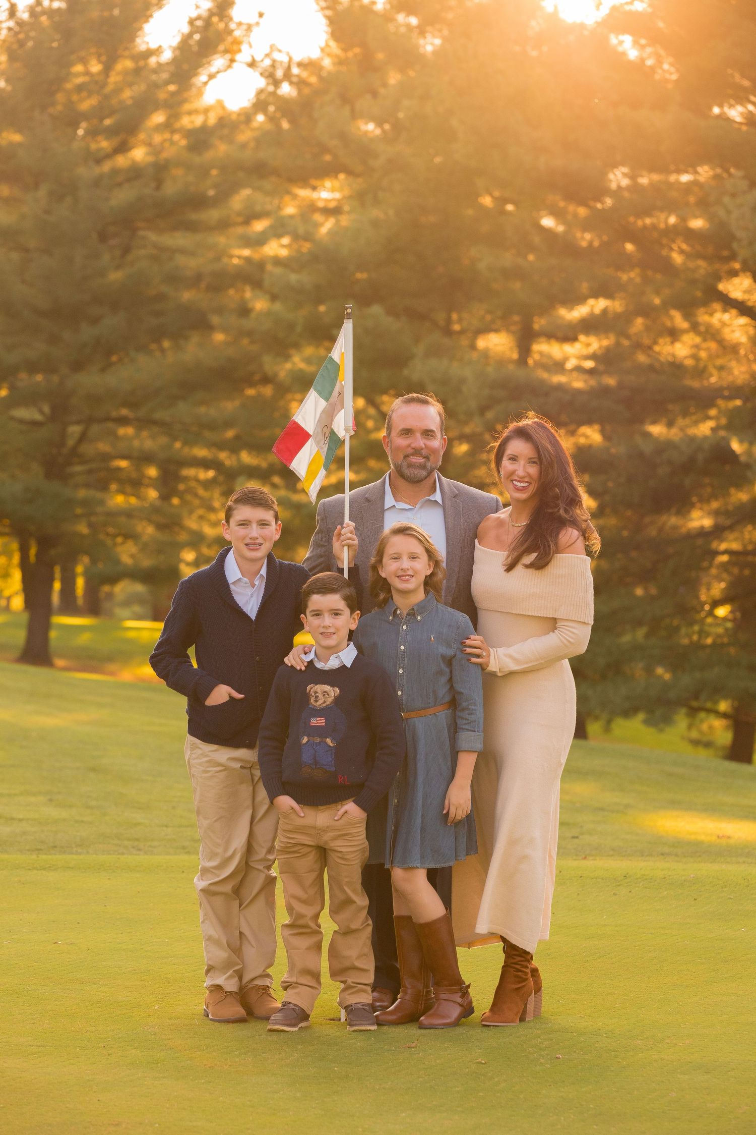 A family poses together on a grassy hill during golden hour sunset in a park setting.