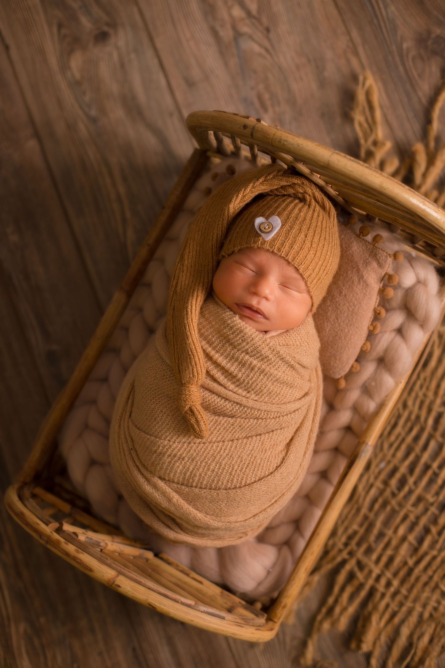 Newborn baby wrapped in tan knit blanket sleeping in wooden basket.