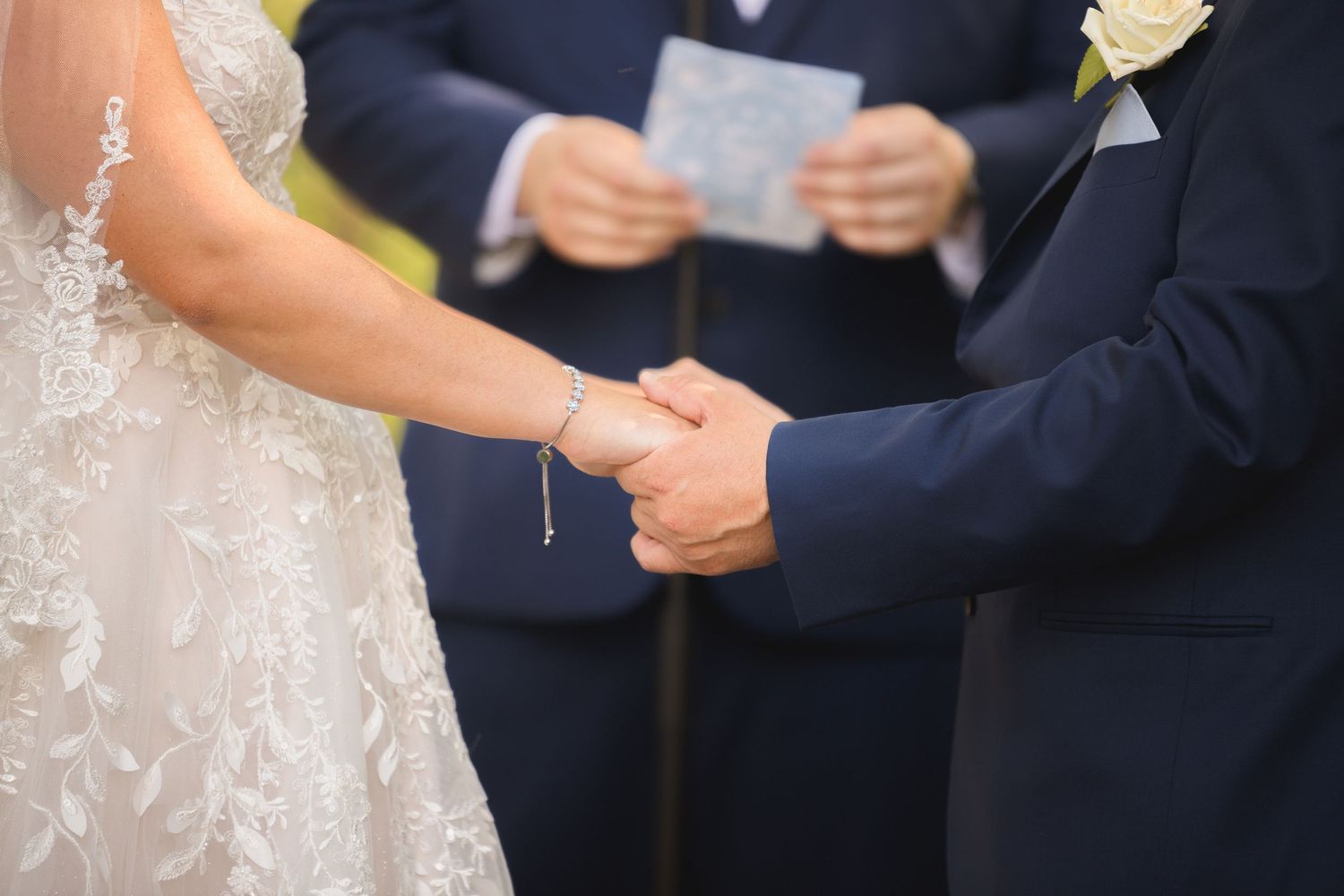 Couple exchanging vows during outdoor wedding ceremony under white draped arch.