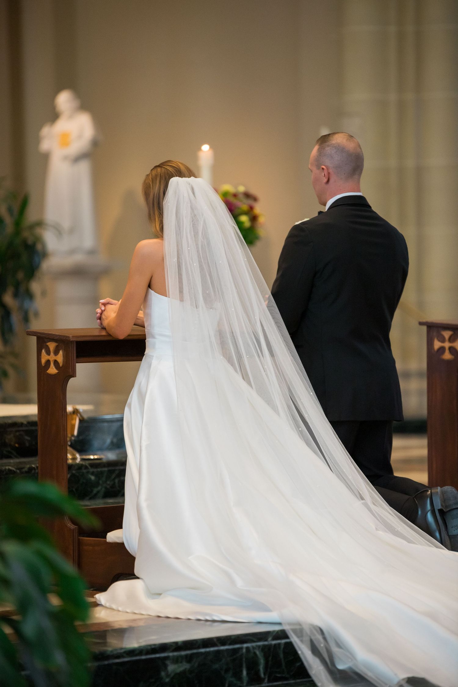 Wedding ceremony in progress with flowing white veil trailing down church aisle.
