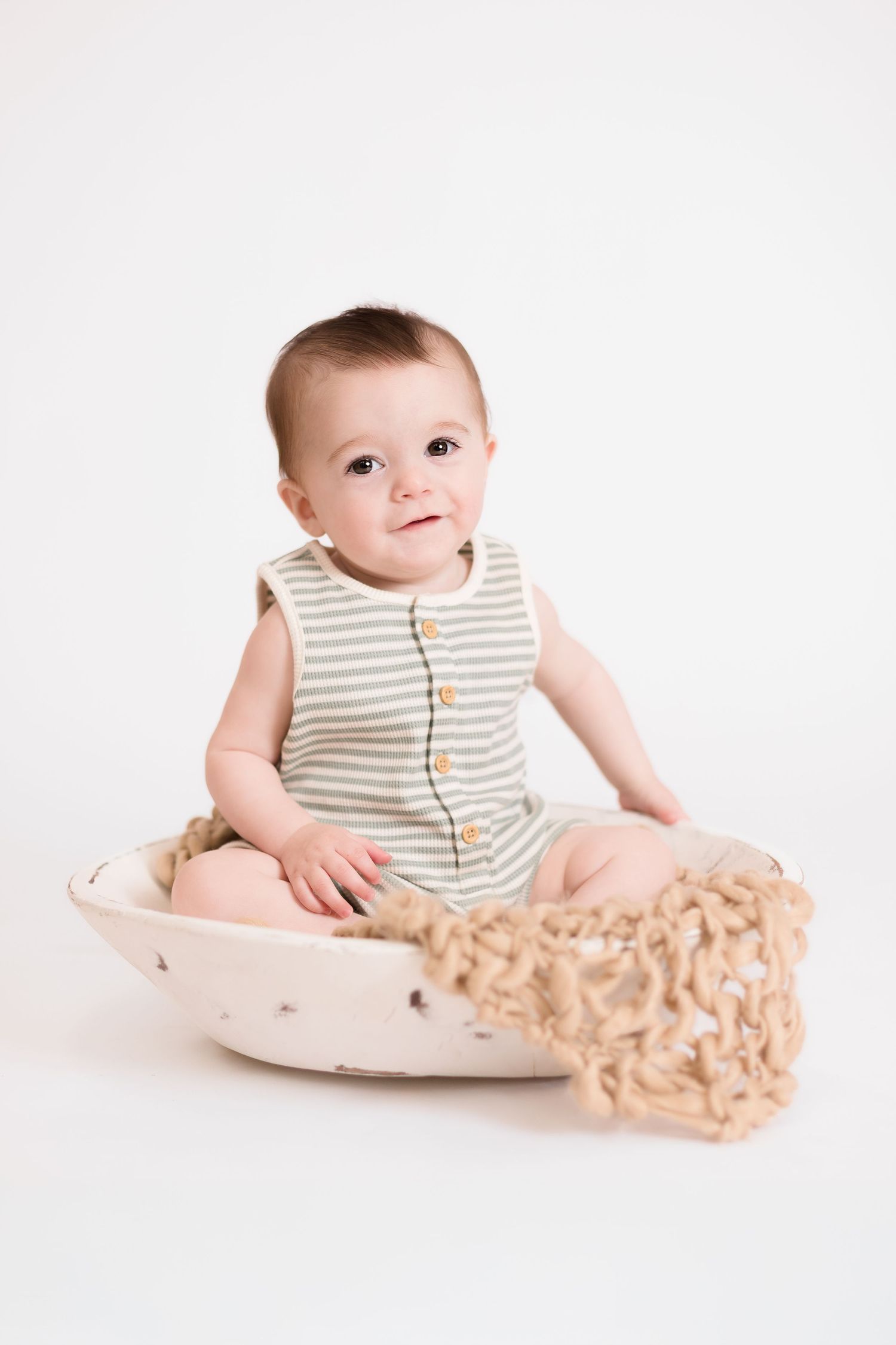 Baby in striped outfit sits in curved wooden rocker against white background.