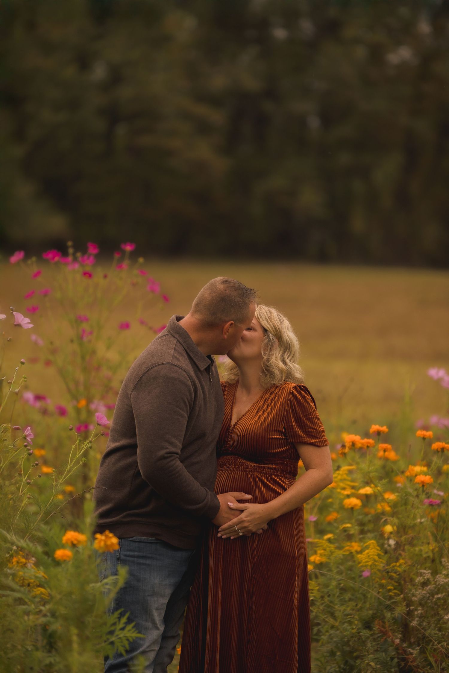 Romantic couple embracing in field of orange and pink wildflowers at sunset.