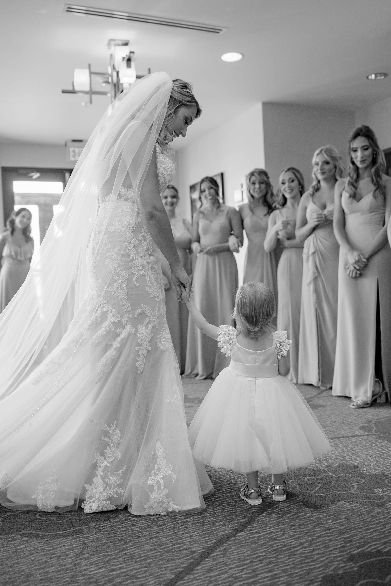 A touching moment between a bride in a lace gown and a small flower girl in a white tulle dress.
