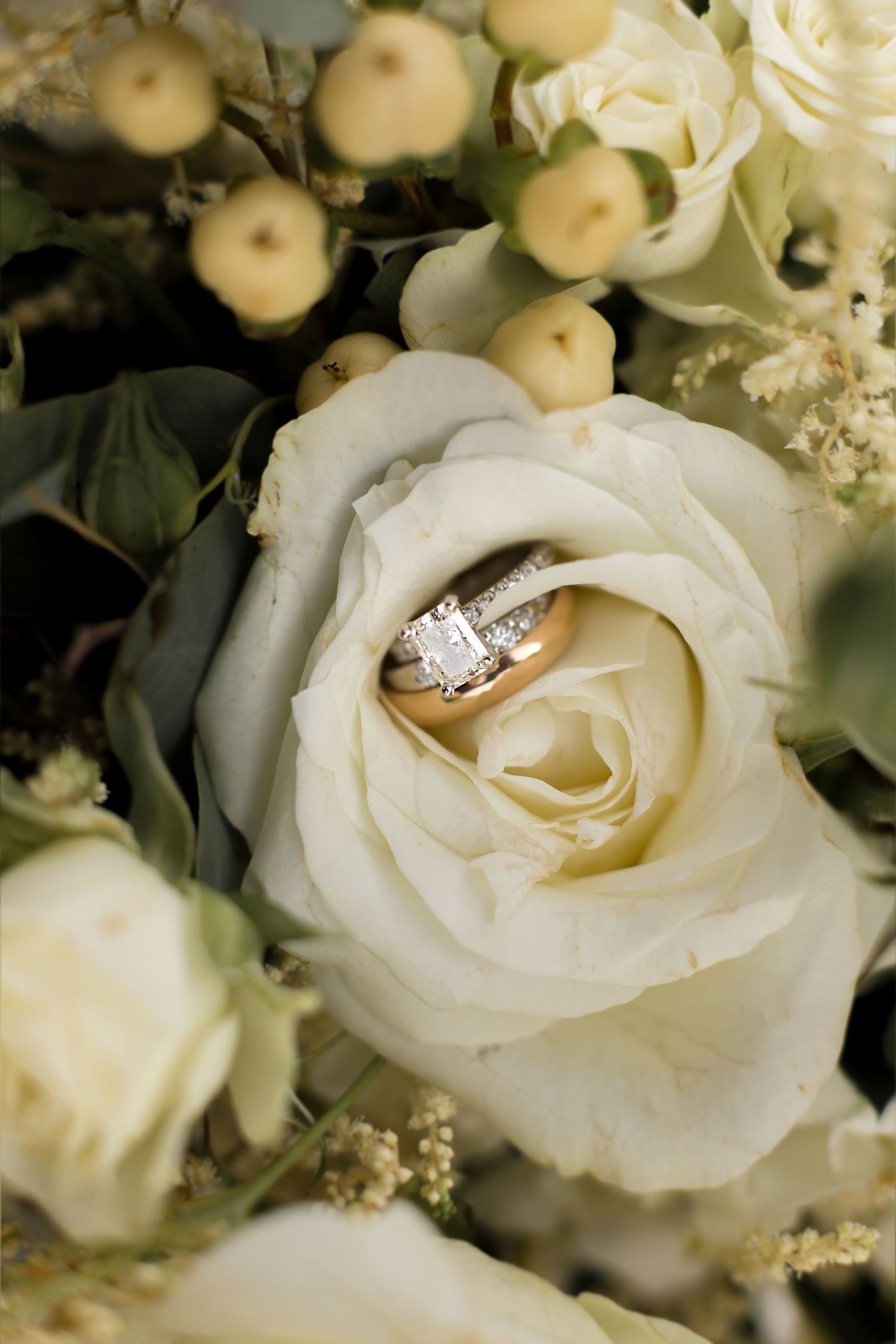 Diamond engagement ring nestled in a white rose bouquet with soft lighting.