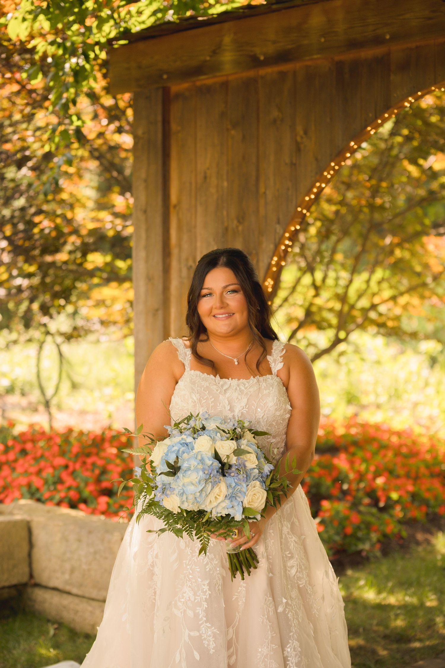 Bride holding beautiful blue and white floral bouquet in sunlit garden setting.