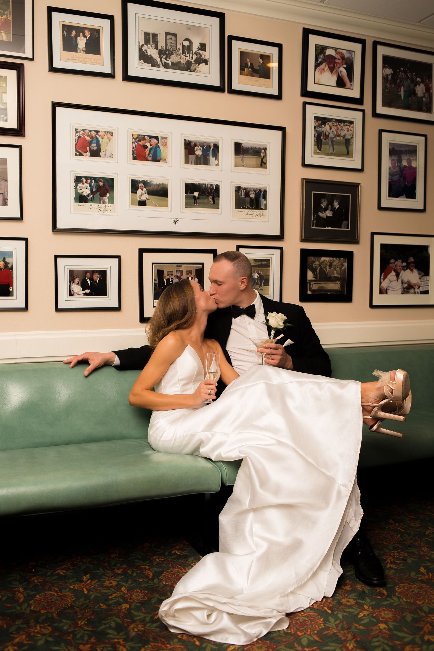 Couple shares intimate moment on vintage green couch surrounded by framed photos.