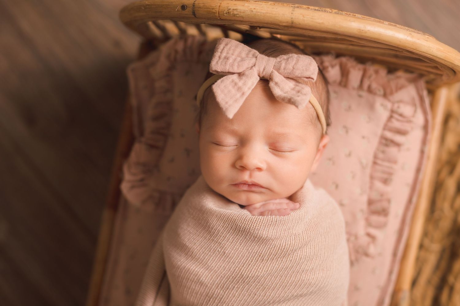 Sleeping newborn wrapped in soft pink swaddle lying in rustic wooden basket.