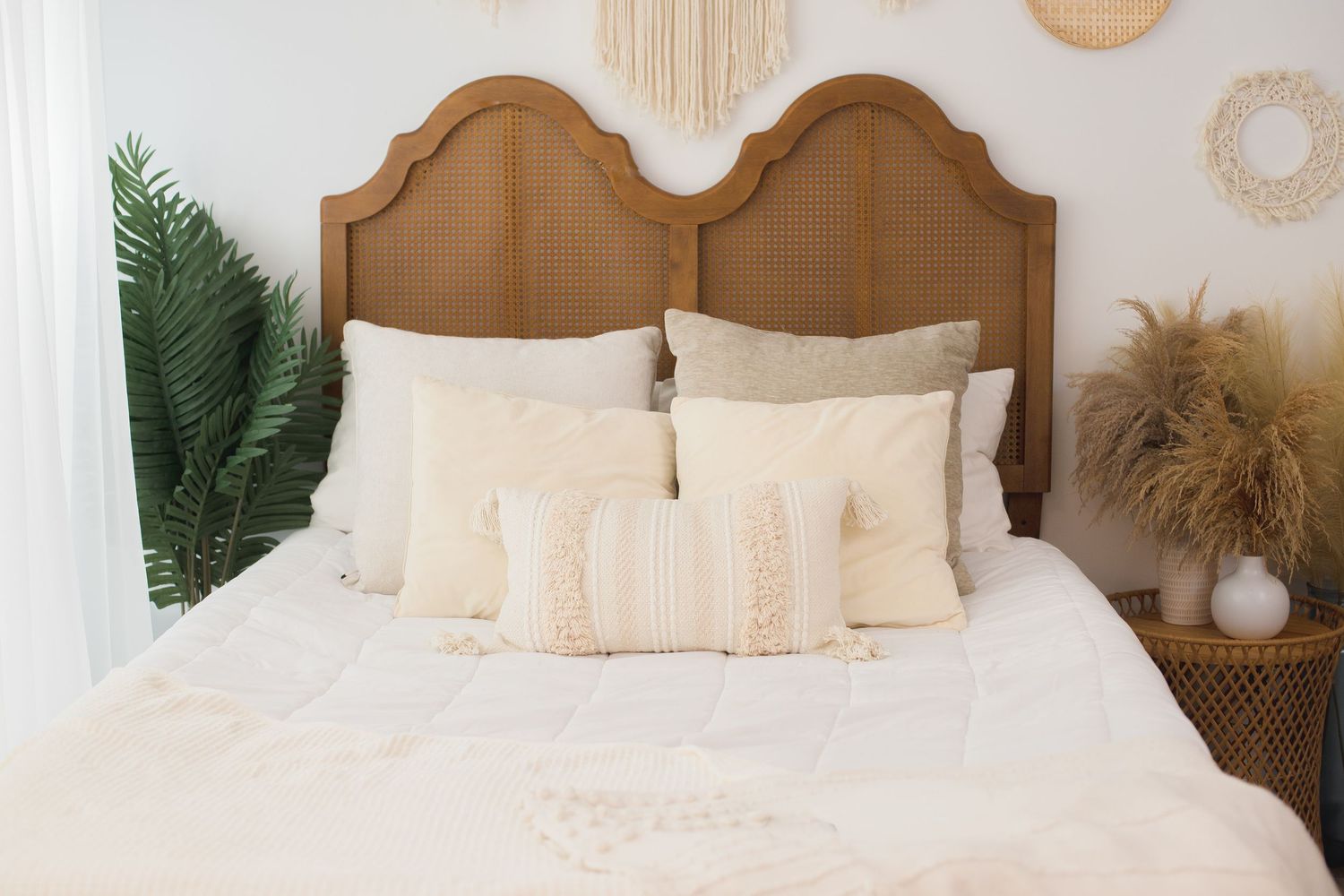 Boho-style bedroom with macrame wall decor, rattan accents, and neutral bedding against a white wall.
