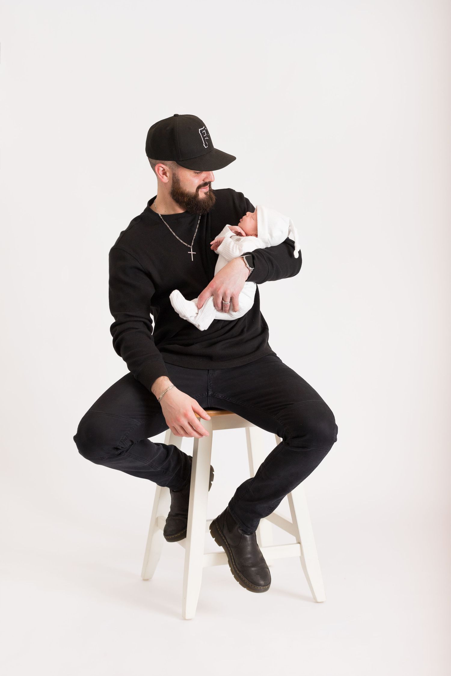 Person wearing all black sits on white chair in three similar poses against white background.
