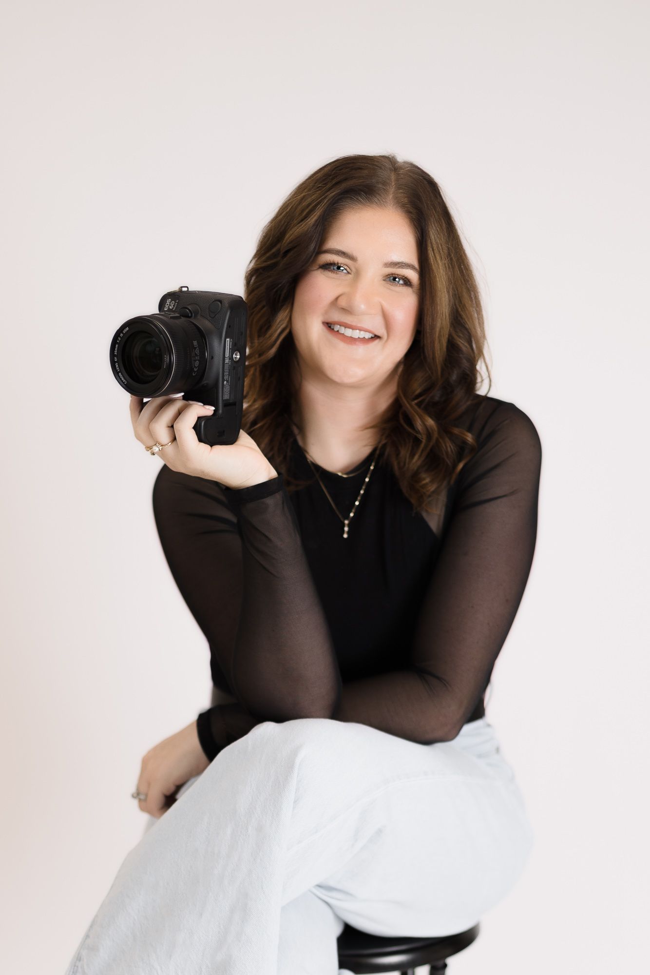 Professional photographer in black top holding camera against white background in studio portrait session.