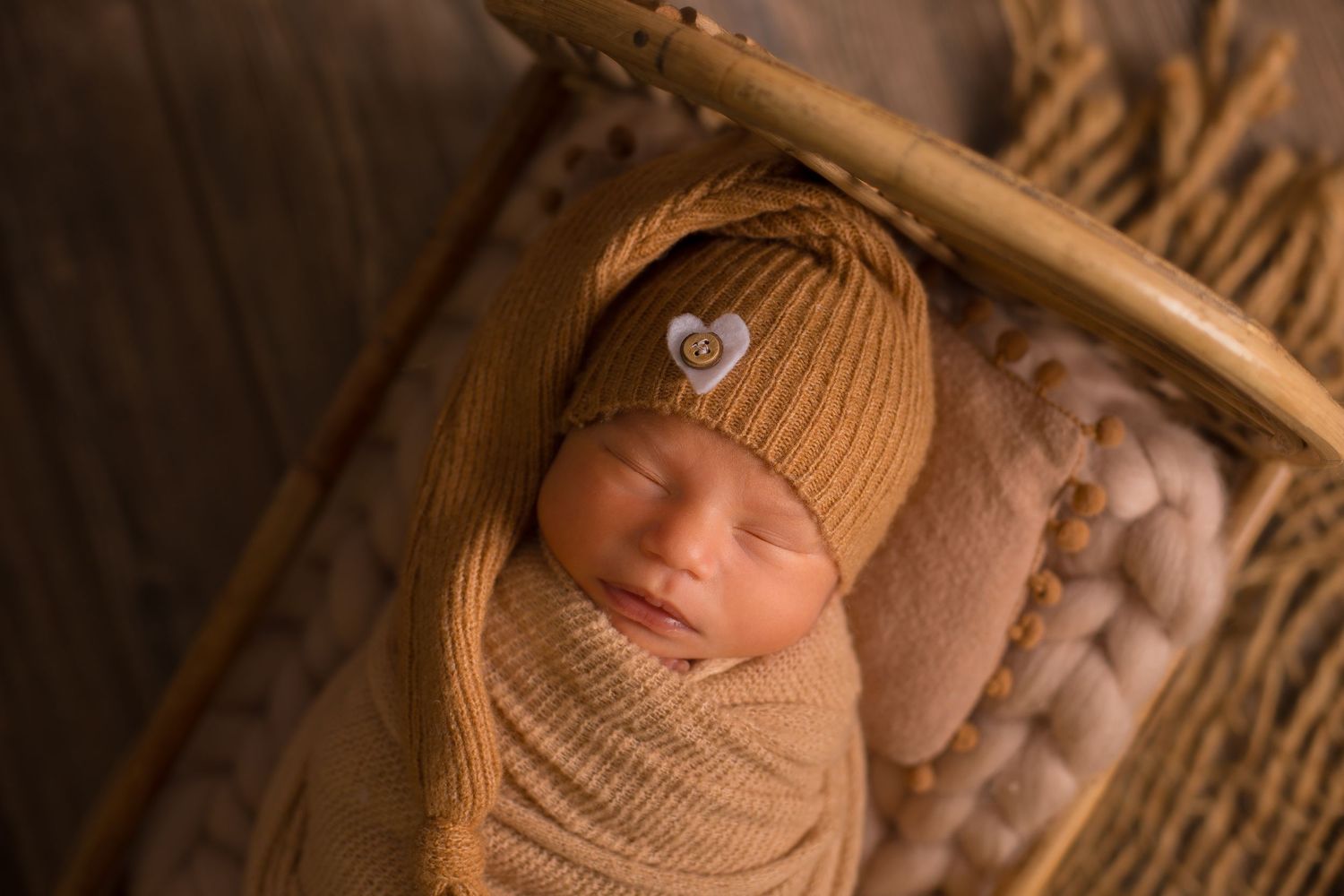 Close-up series of sleeping newborn in tan wrap on textured wooden surface.