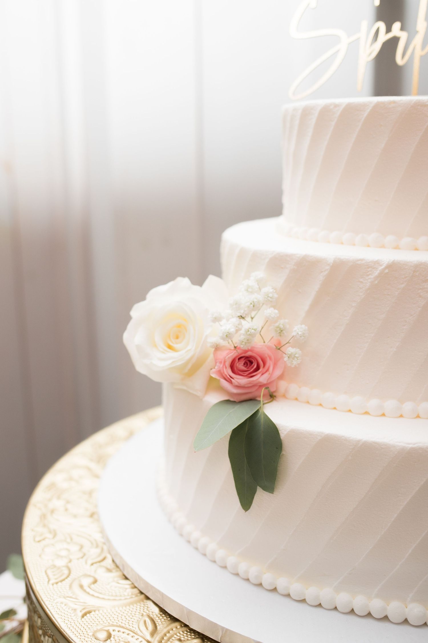 Elegant white wedding cake decorated with delicate pink and cream roses on a gold cake stand.
