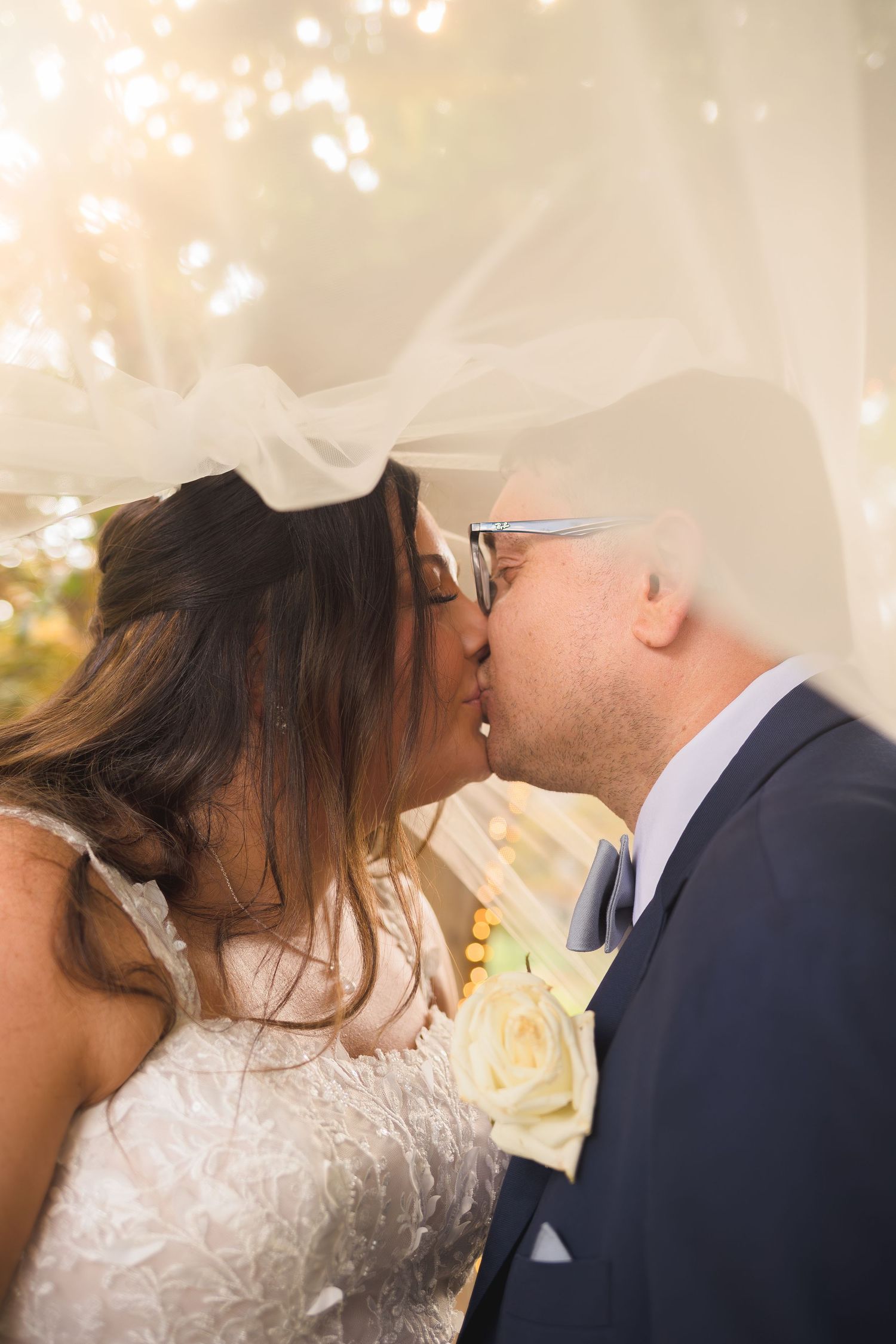 Intimate moment between newlyweds under twinkling lights and white veil.