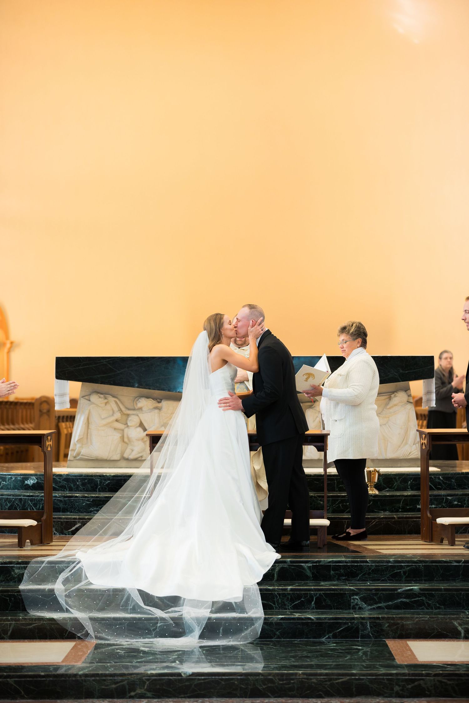 A wedding couple descends church steps while the bride's veil flows dramatically behind them.
