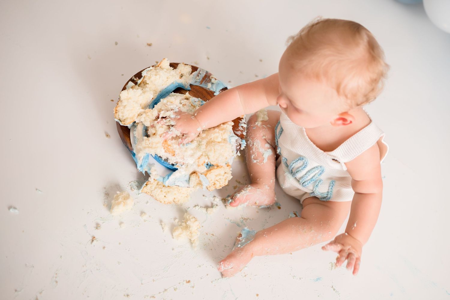 Messy cake smash aftermath with frosting scattered on white floor.