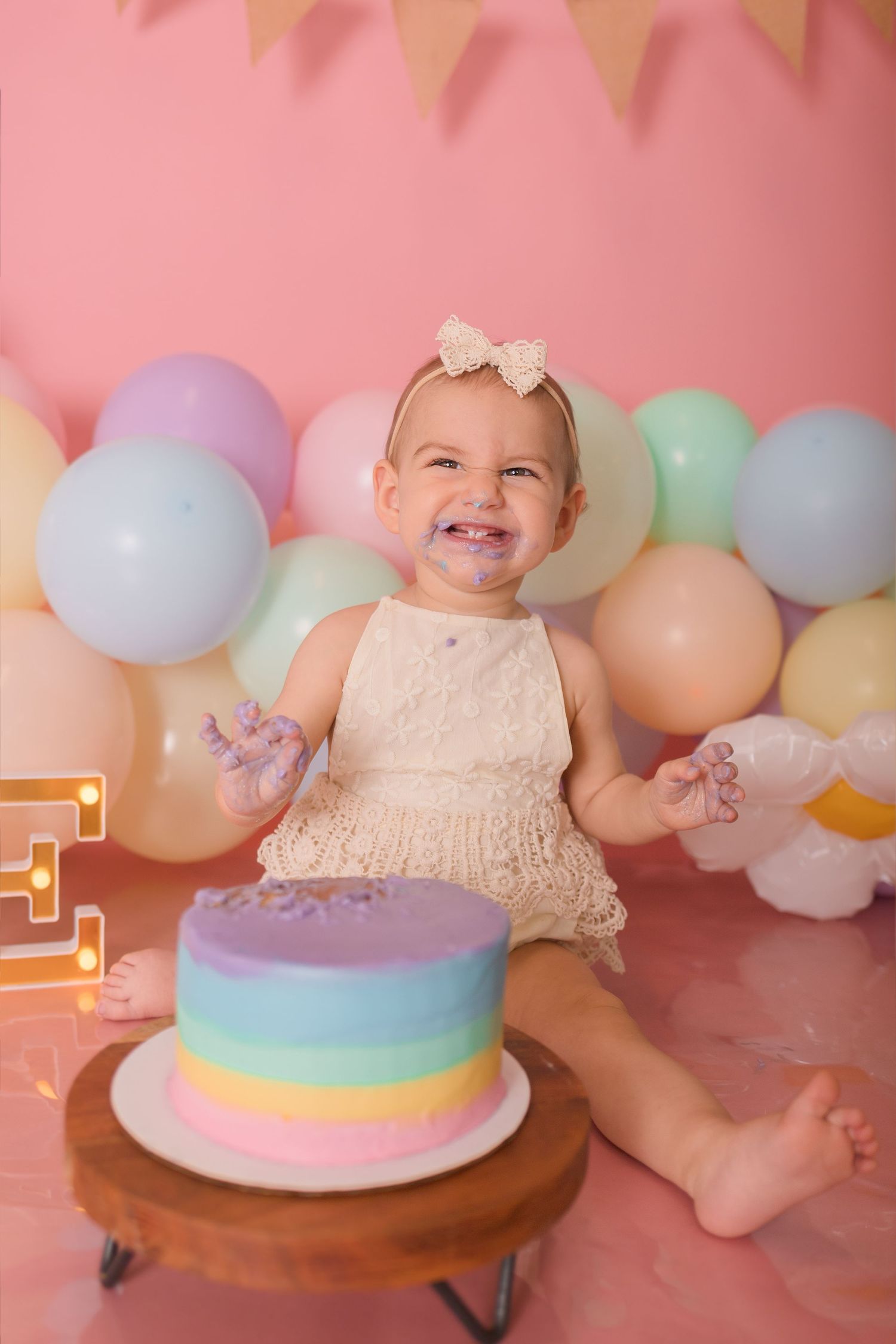 A joyful celebration scene with a rainbow cake and colorful balloon arch backdrop.