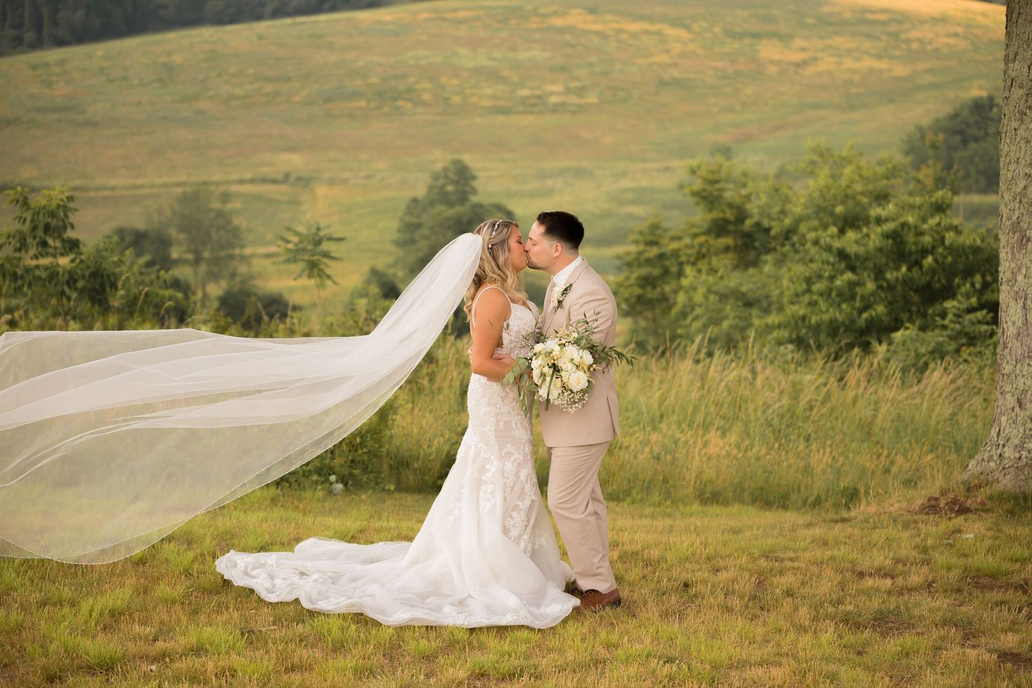 Bride's veil flows in the wind during outdoor portrait session on rolling hills.