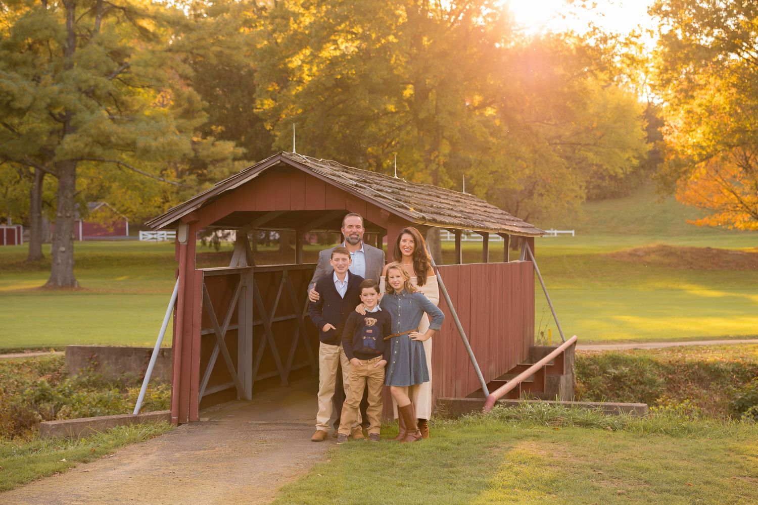 A rustic red barn provides a backdrop for a sunset gathering in a pastoral setting.