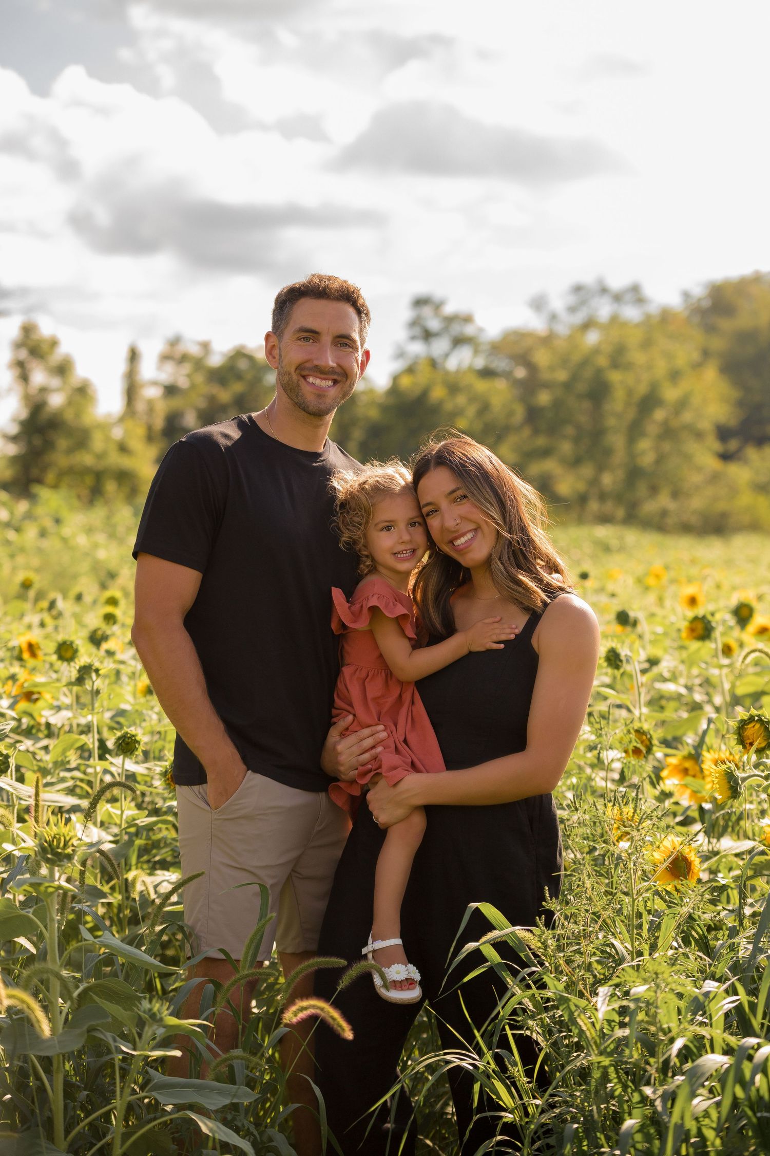 A family embraces while standing in a beautiful sunflower field on a cloudy day.