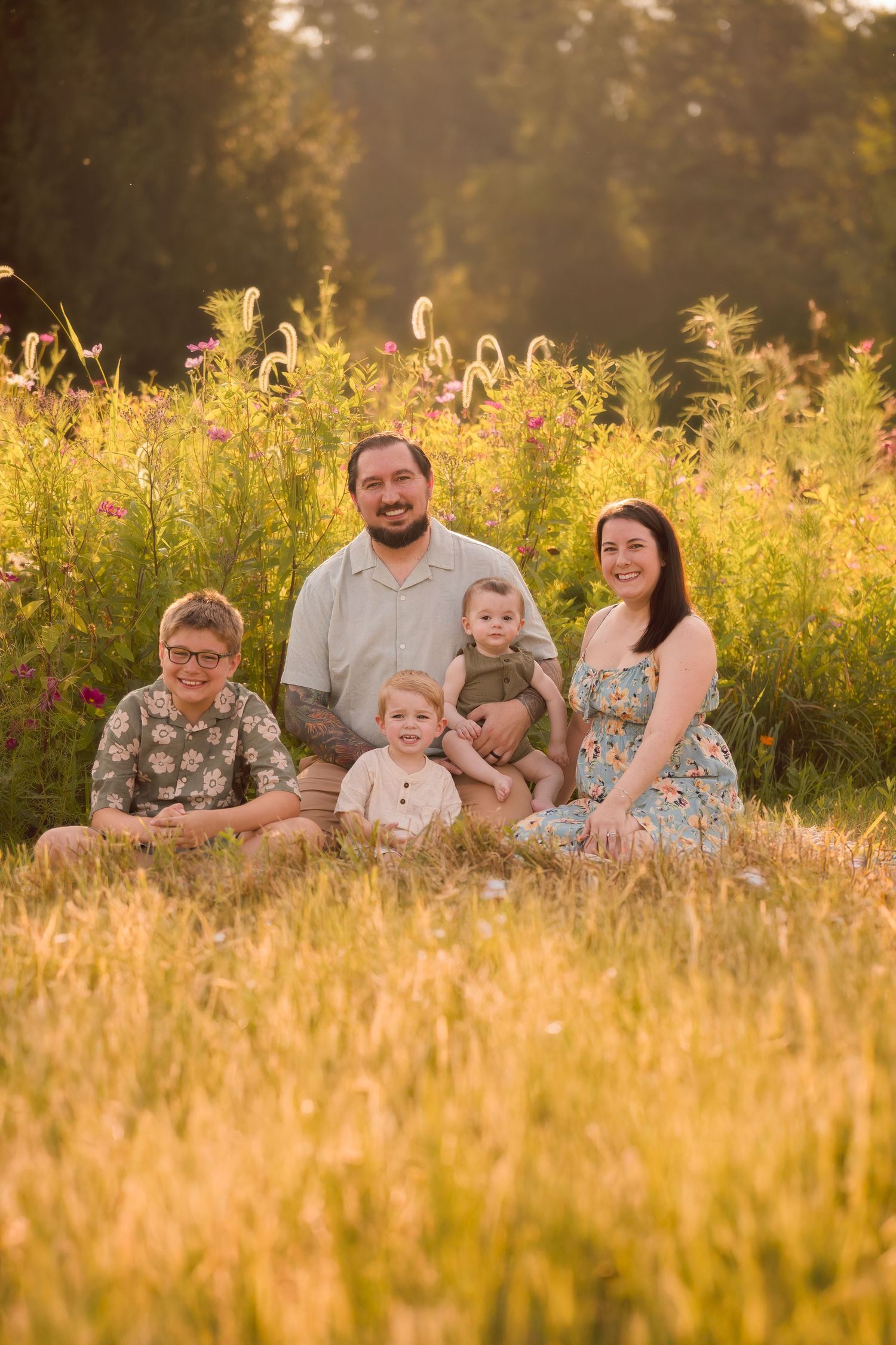 Family sitting together in golden sunlit meadow during sunset photo session.