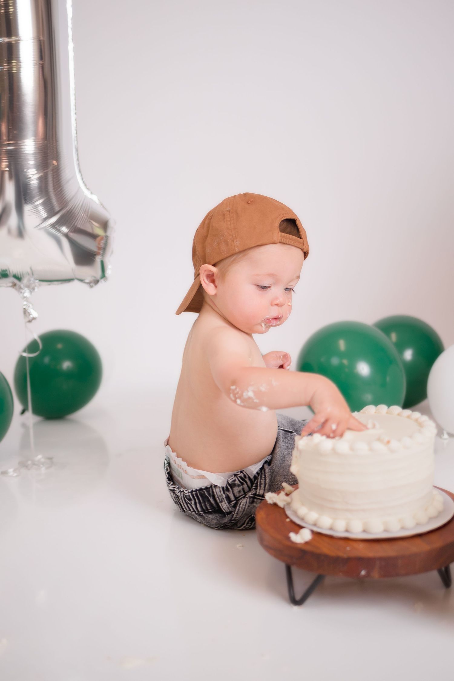 A cake smash photo session with silver balloons and green decorations.