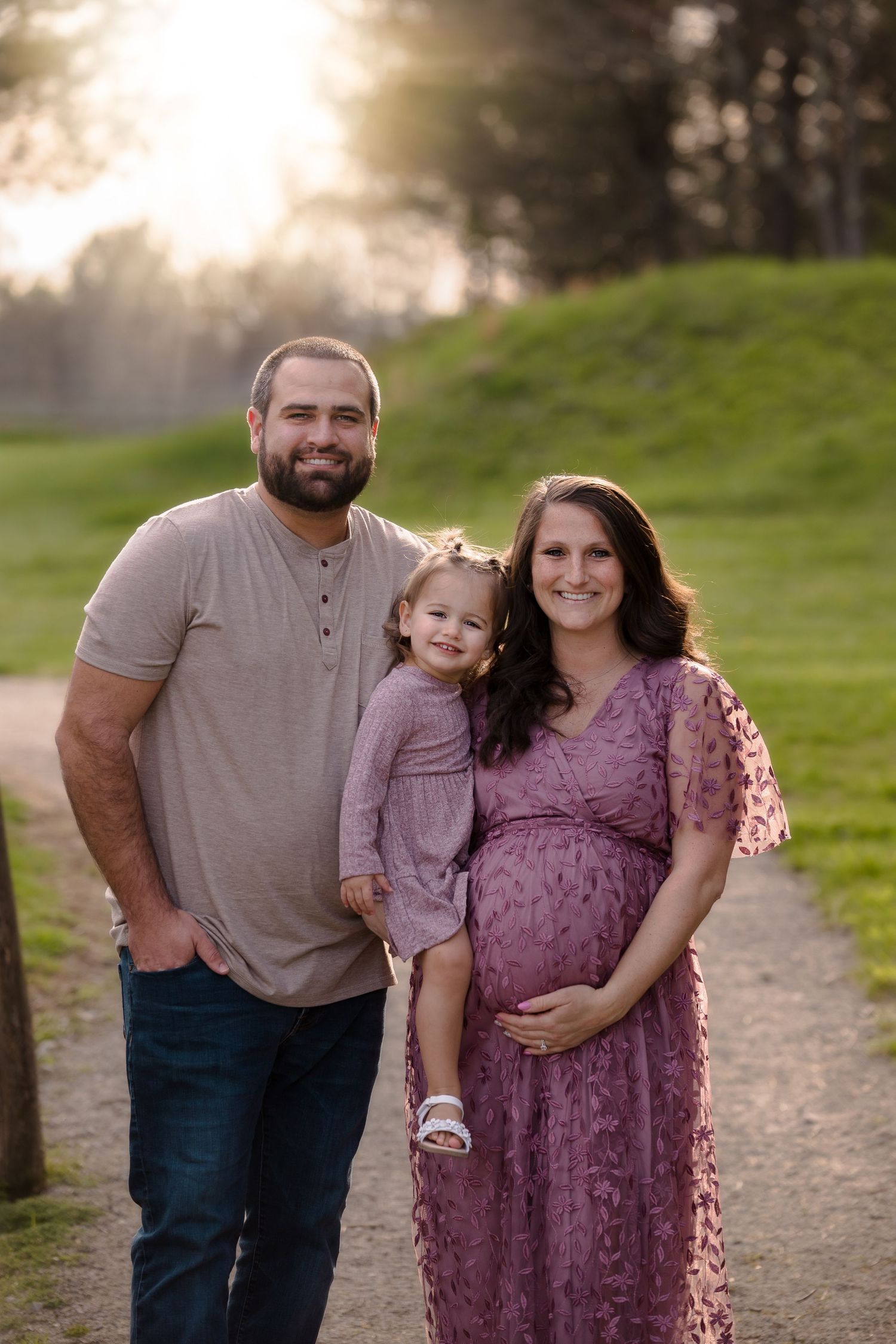 A family shares a warm moment at sunset on a dirt path surrounded by green hills.