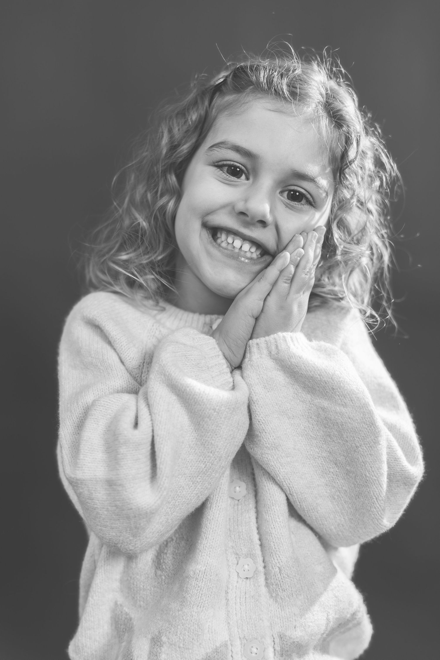 A series of black and white photos showing a child in a white sweater making playful expressions and gestures.