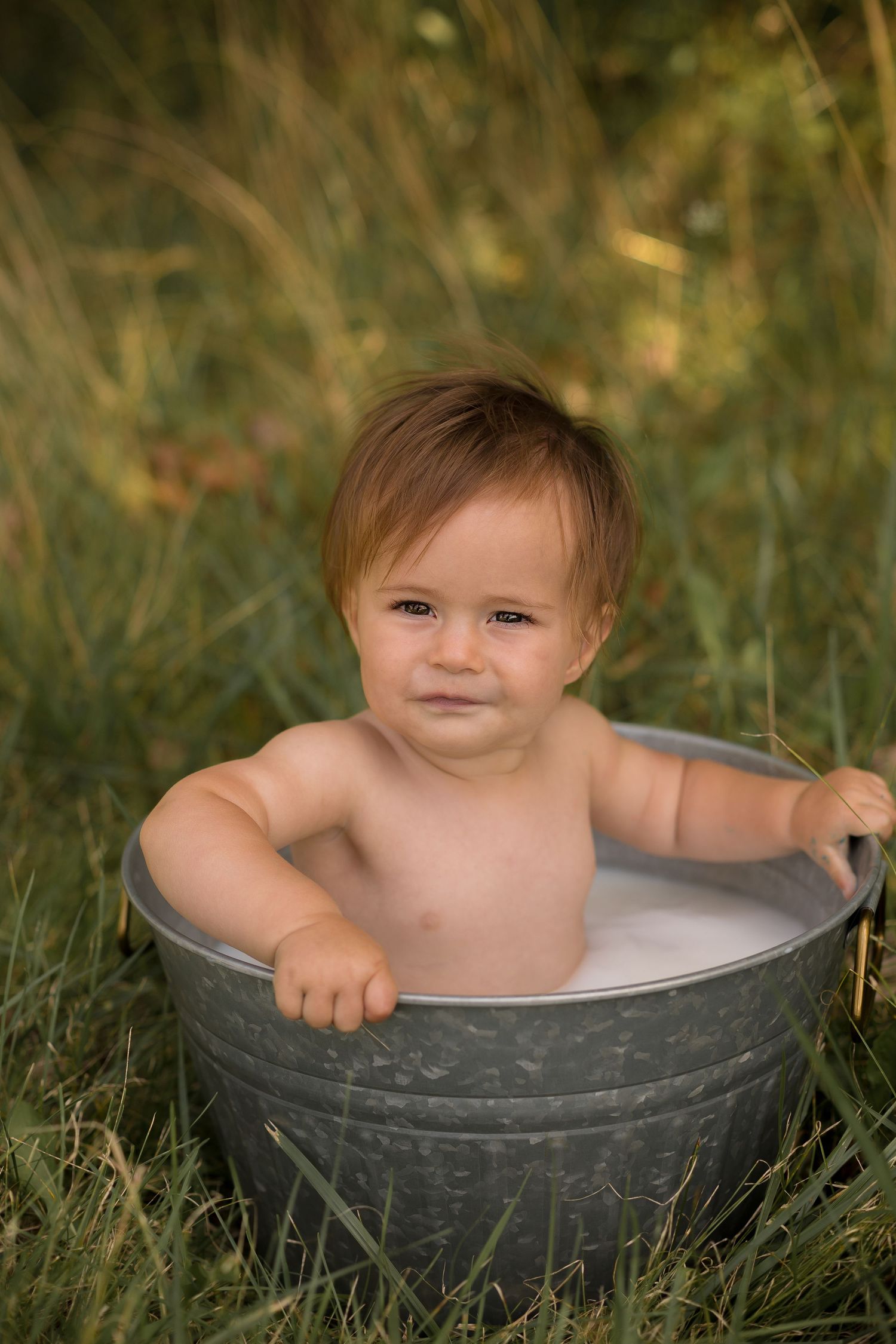 Rustic milk bath photography featuring galvanized metal tub in tall grass setting.