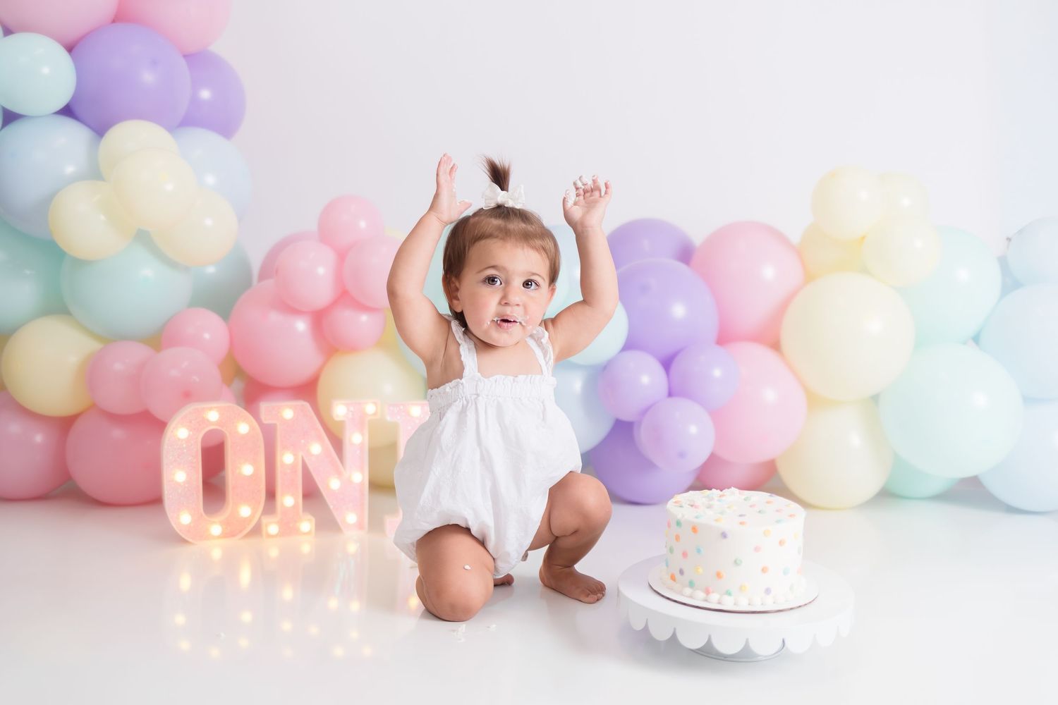 A first birthday celebration setup with pastel balloons and lit-up letters.