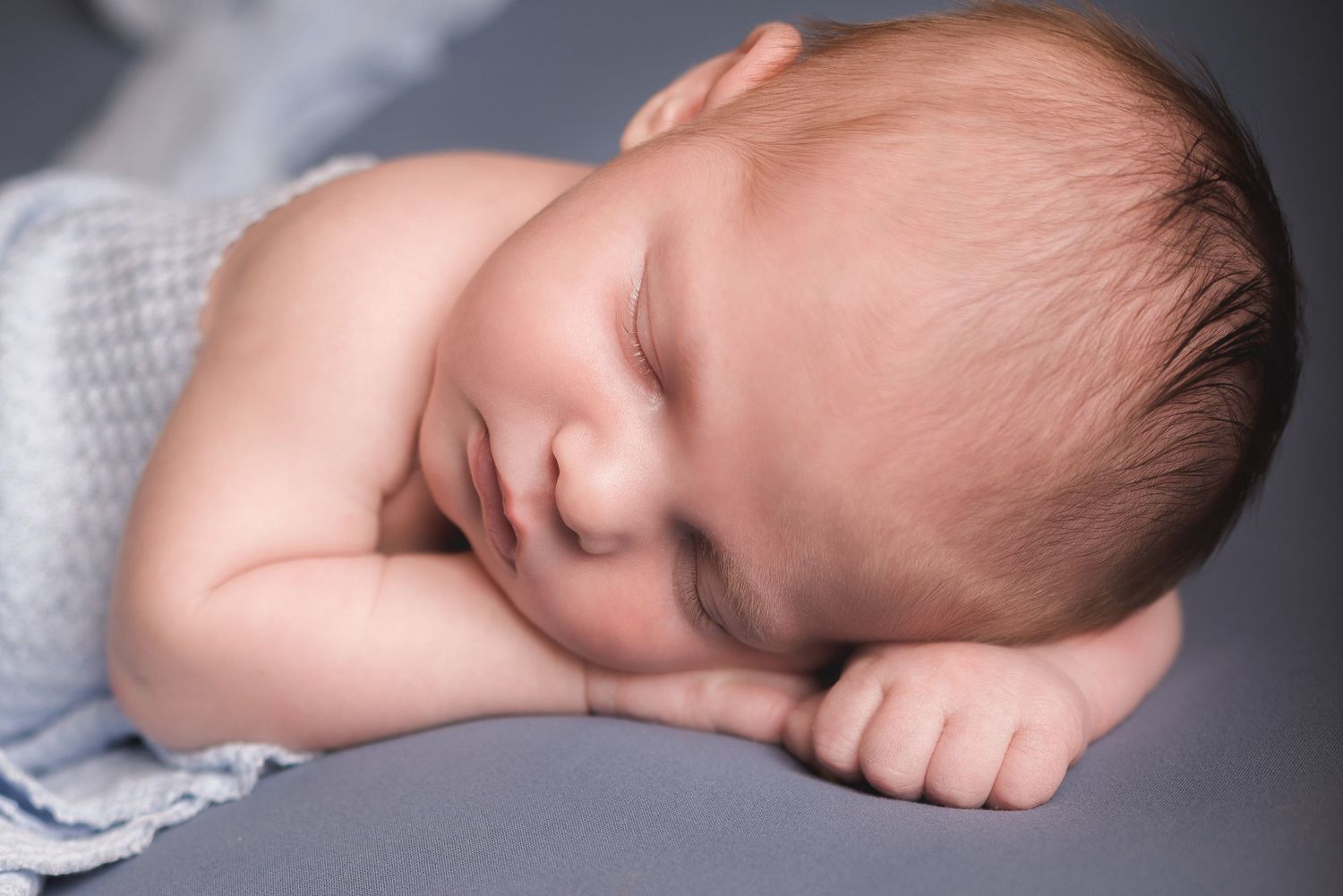 Artistic series of sleeping newborn captured in soft light against dark background.