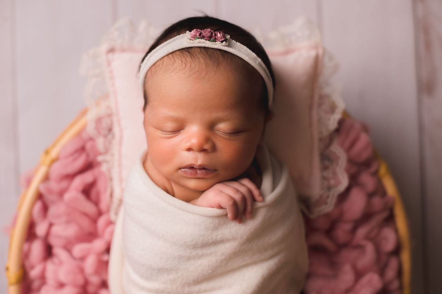 Professional newborn portrait with white wrap against pink textured background.