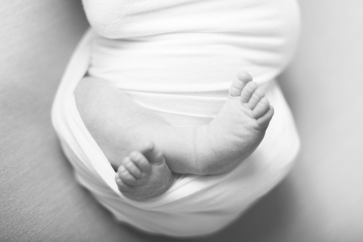 Close-up black and white photo of tiny baby feet wrapped in soft white fabric.