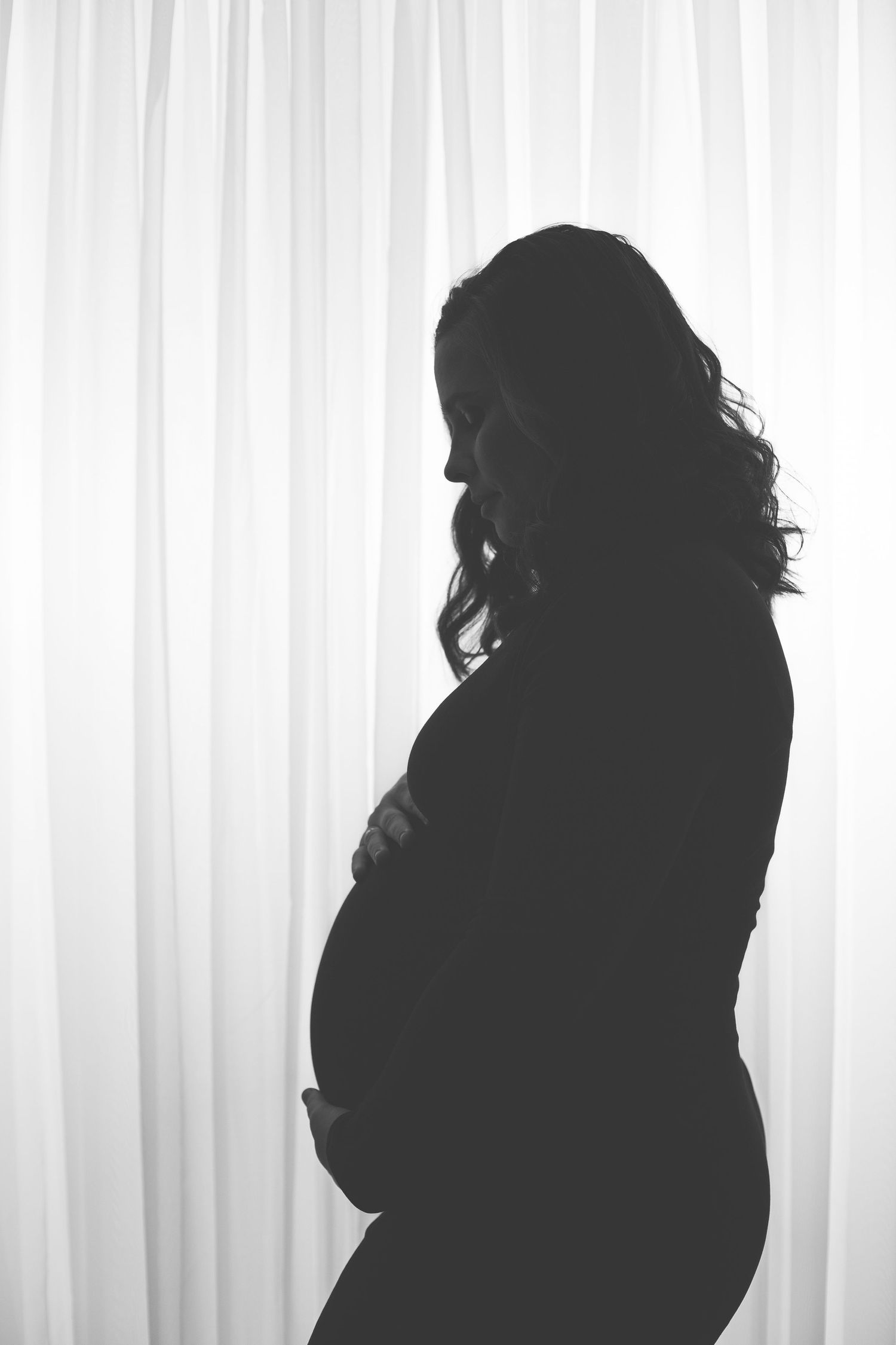 Artistic silhouette maternity portraits against white curtained background.