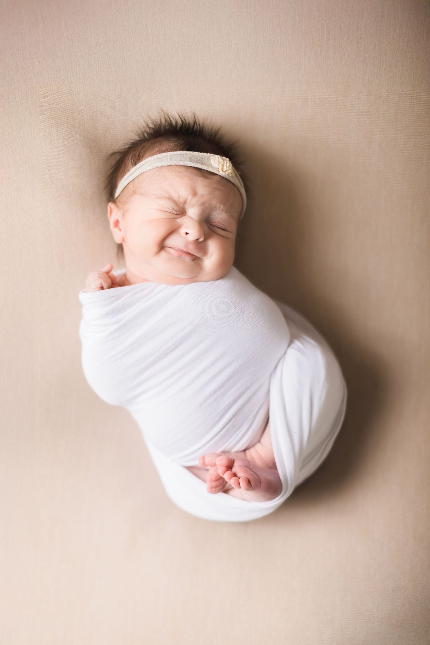 A series of newborn baby photos showing a sleeping infant swaddled in white against a neutral beige background.