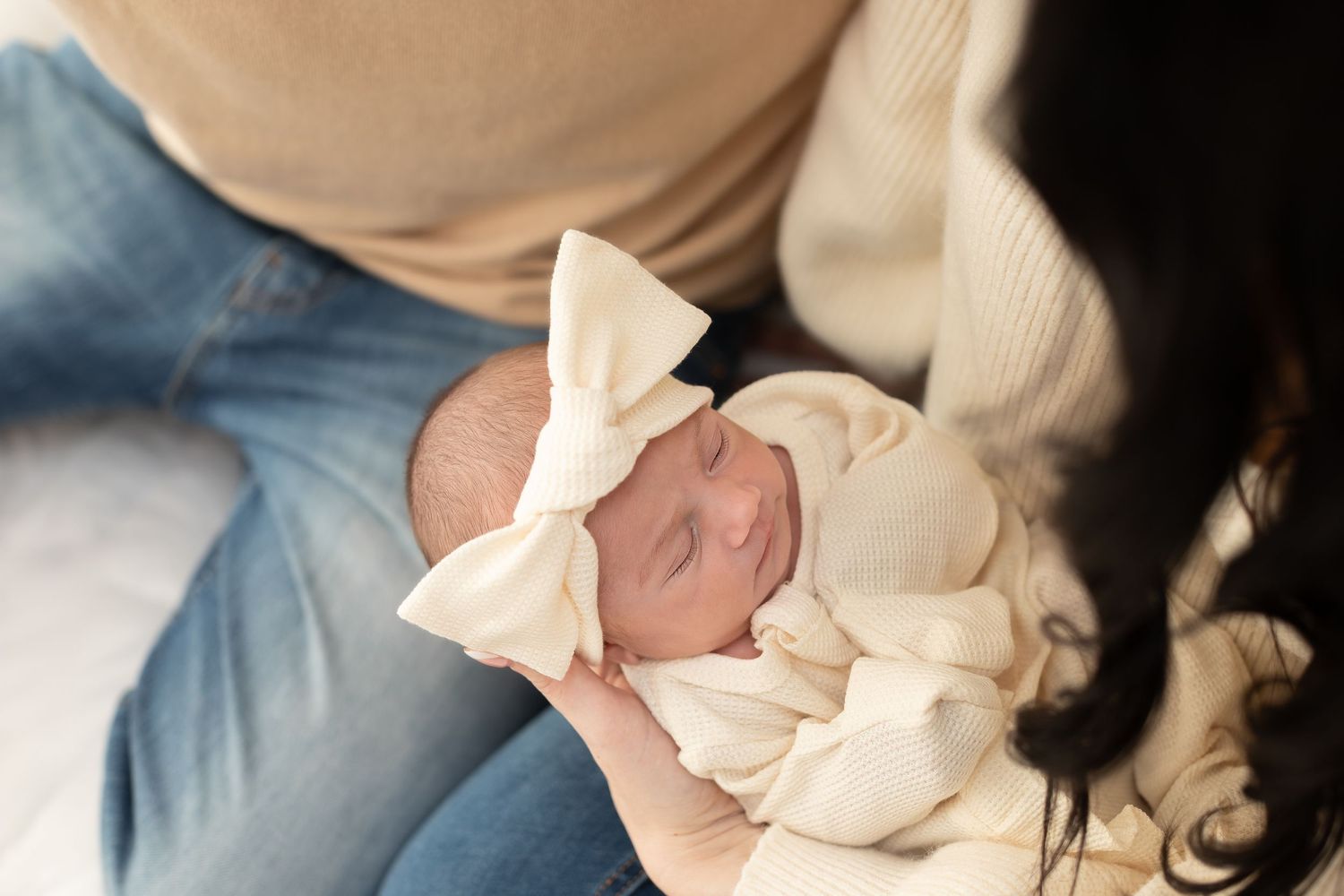 Tender moment with newborn baby wrapped in cream blanket during lifestyle photo session.