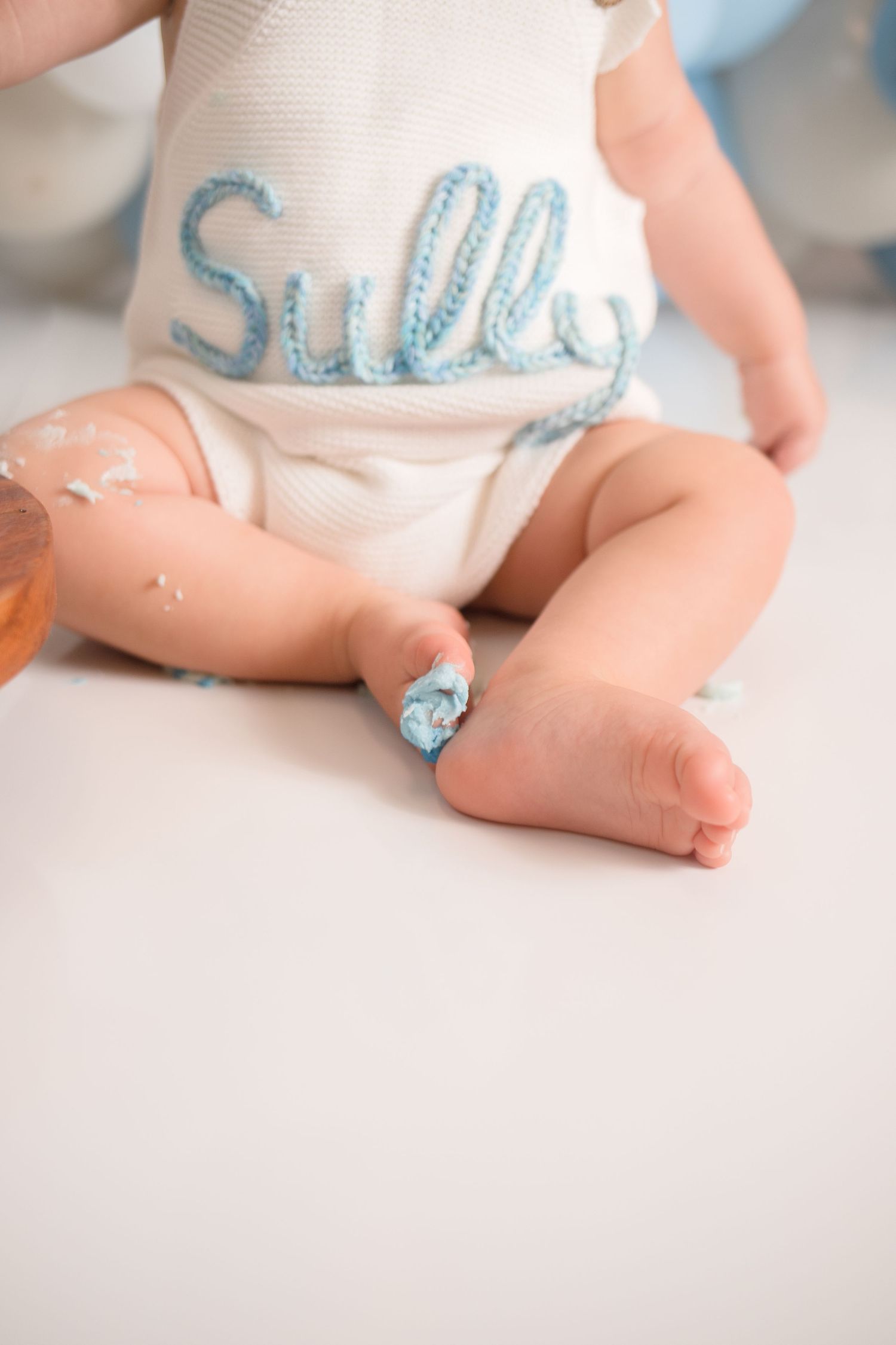 Close-up of baby wearing white outfit with blue lettering during first birthday shoot.