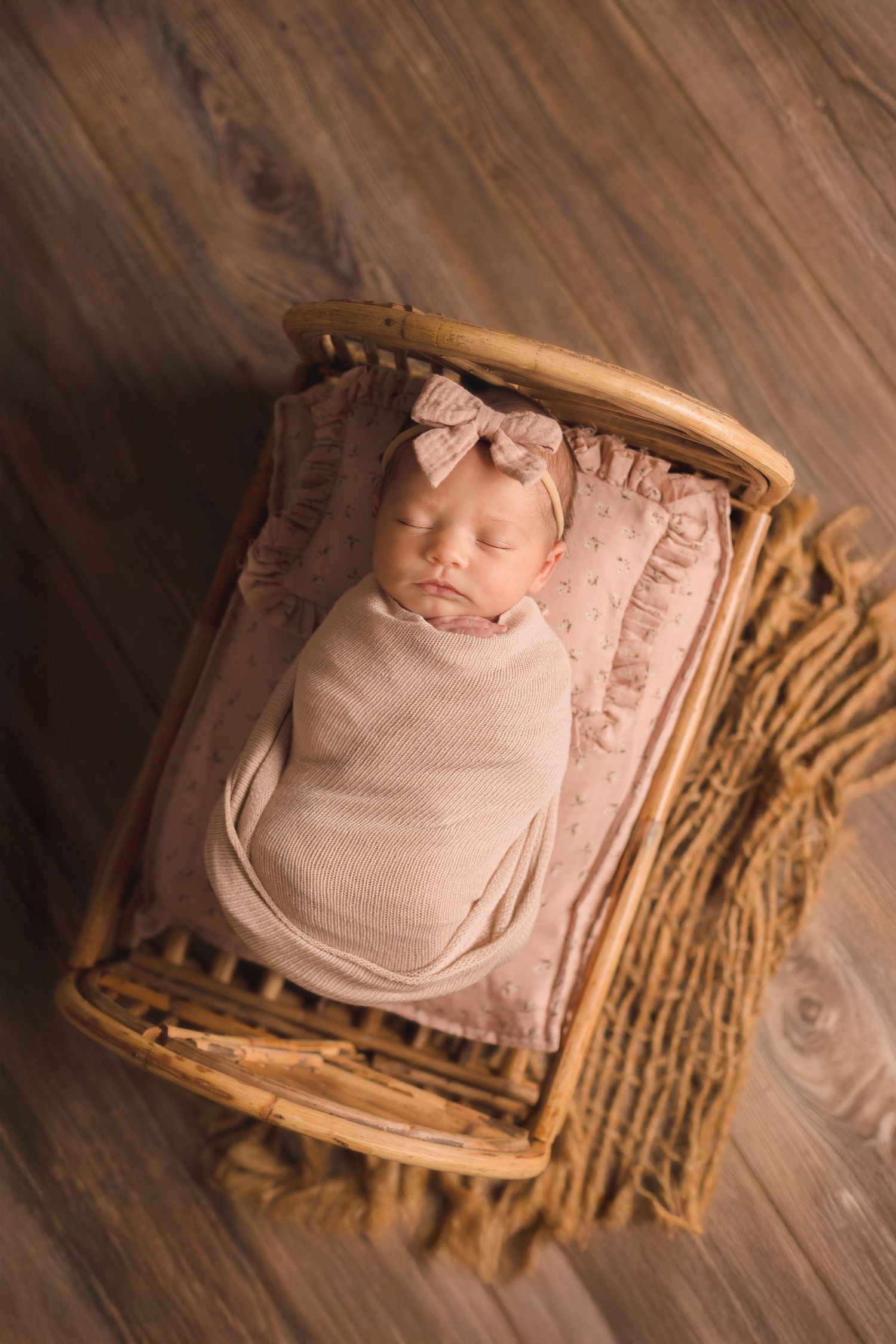 Newborn photography setup with baby wrapped in pink blanket resting in wooden basket on hardwood floor.