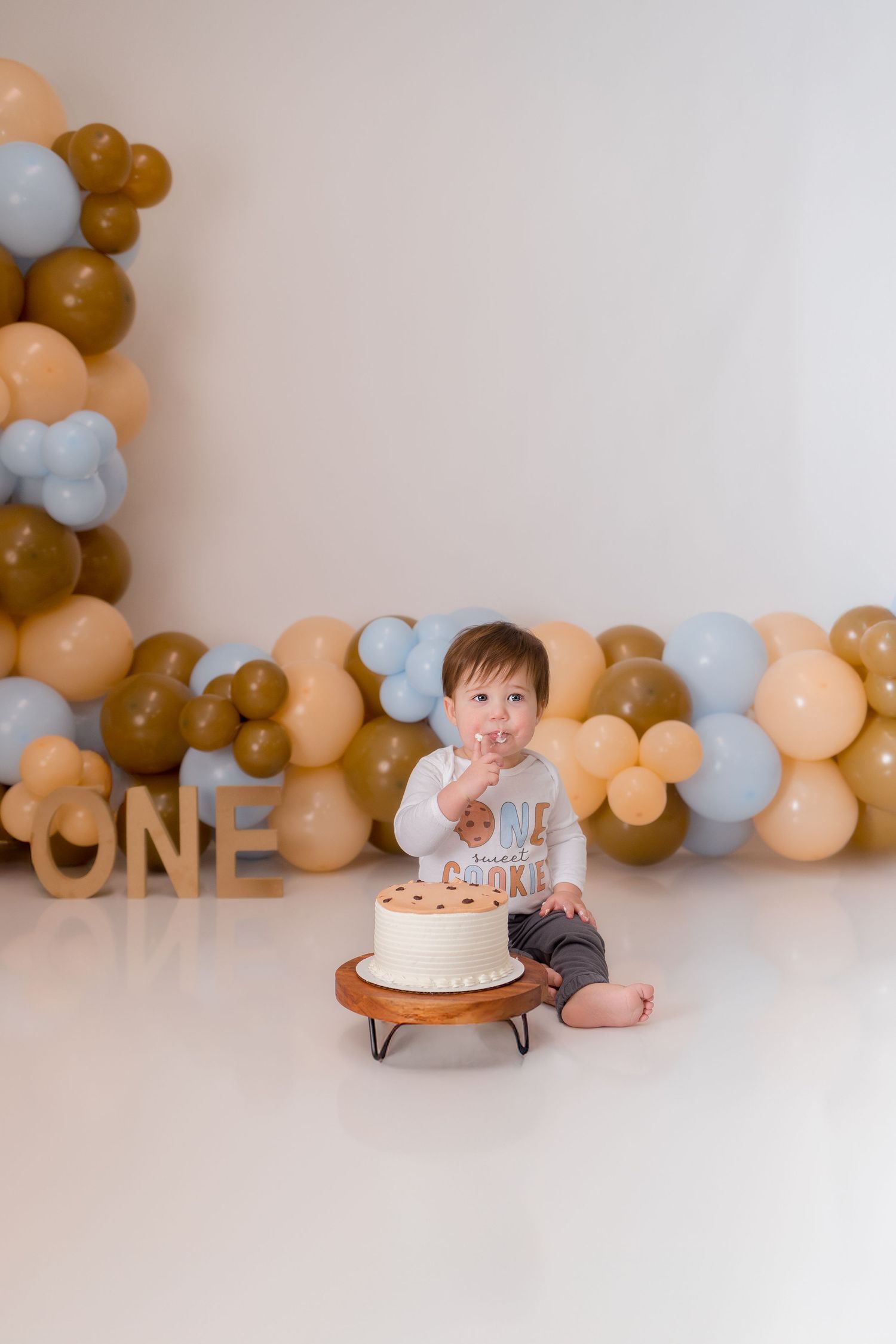 White birthday cake displayed with balloon decorations and 'ONE' sign for first birthday celebration.