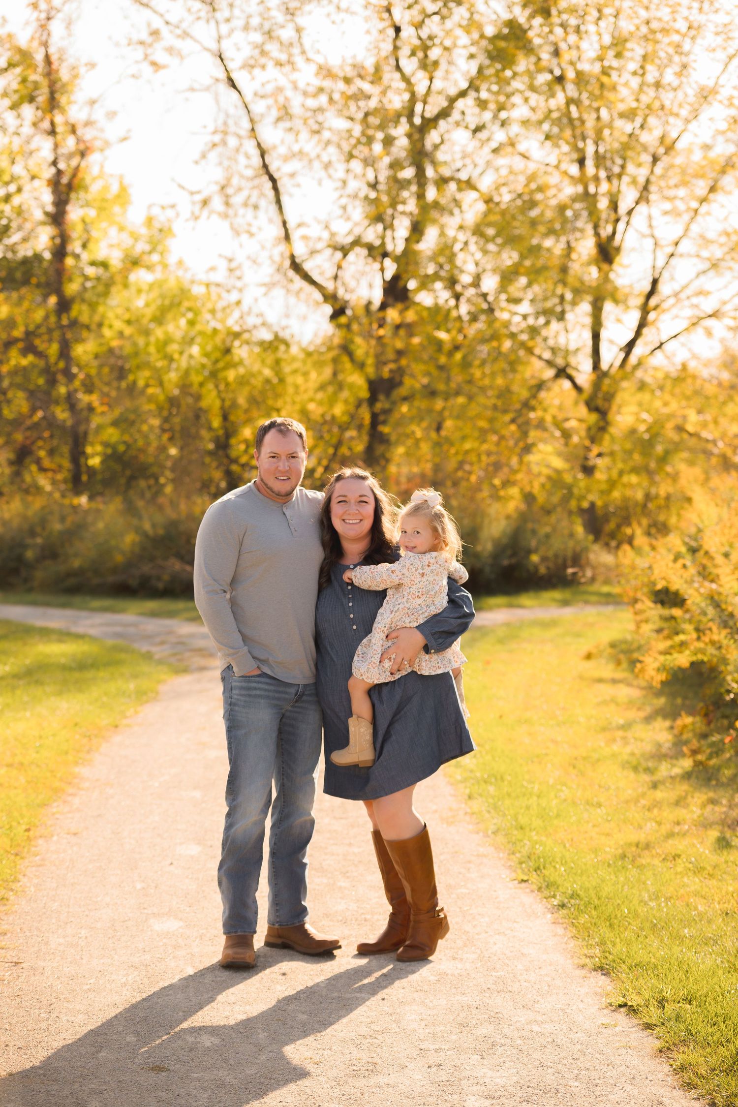 Family of three poses on a sunlit autumn path during golden hour.