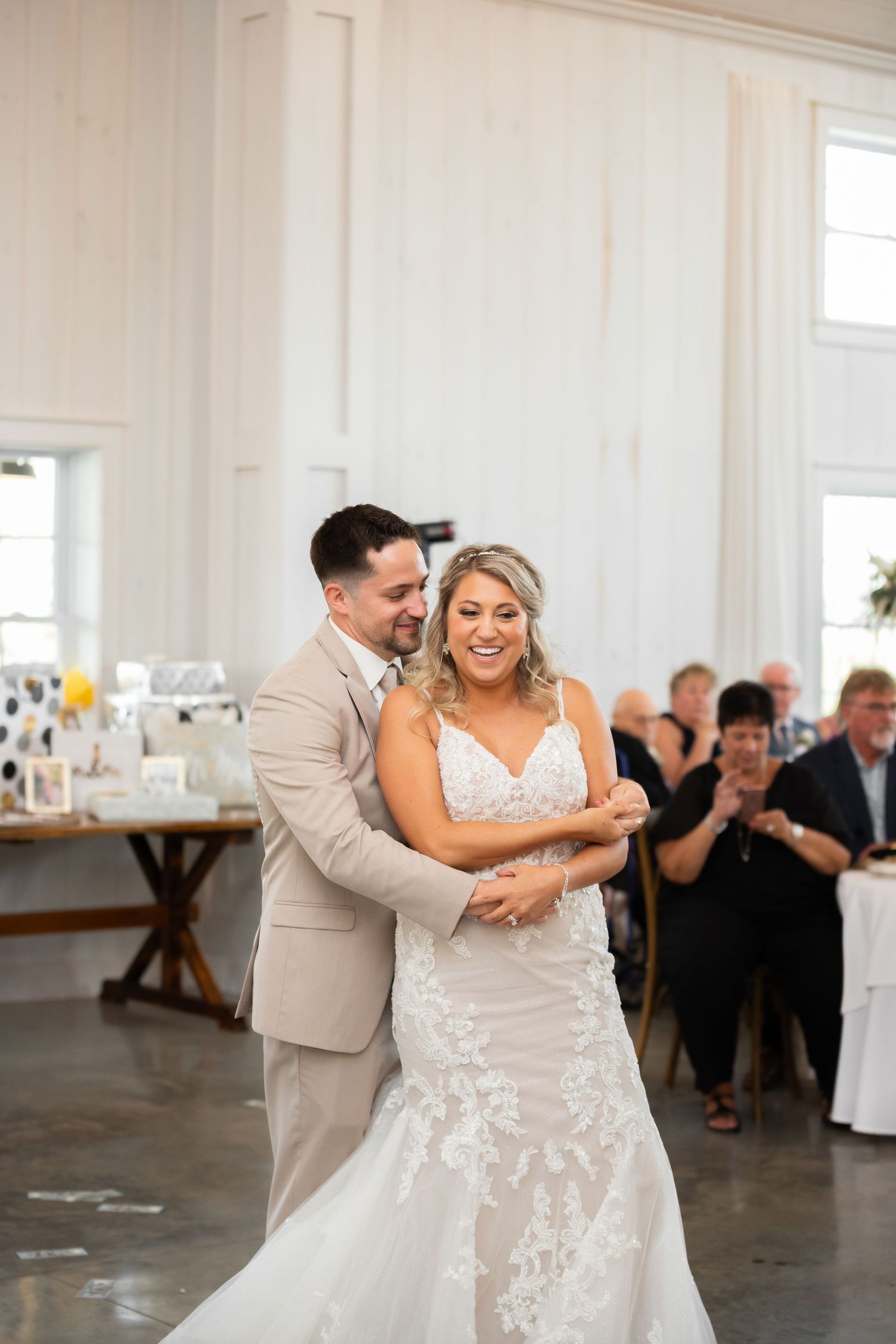 A newlywed couple shares a tender moment during their first dance in a bright reception venue.