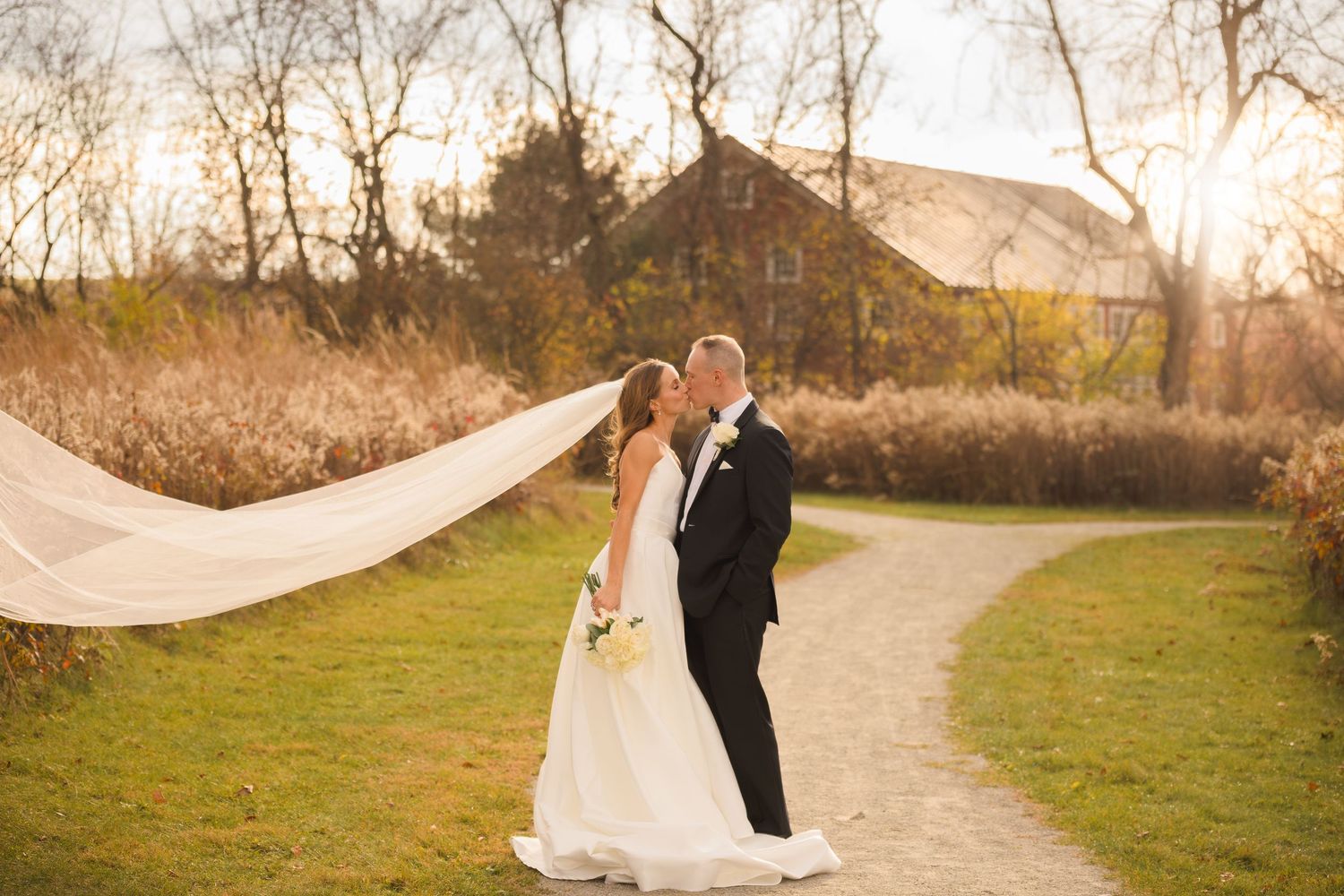 Wedding couple poses on outdoor path during golden hour with flowing veil.