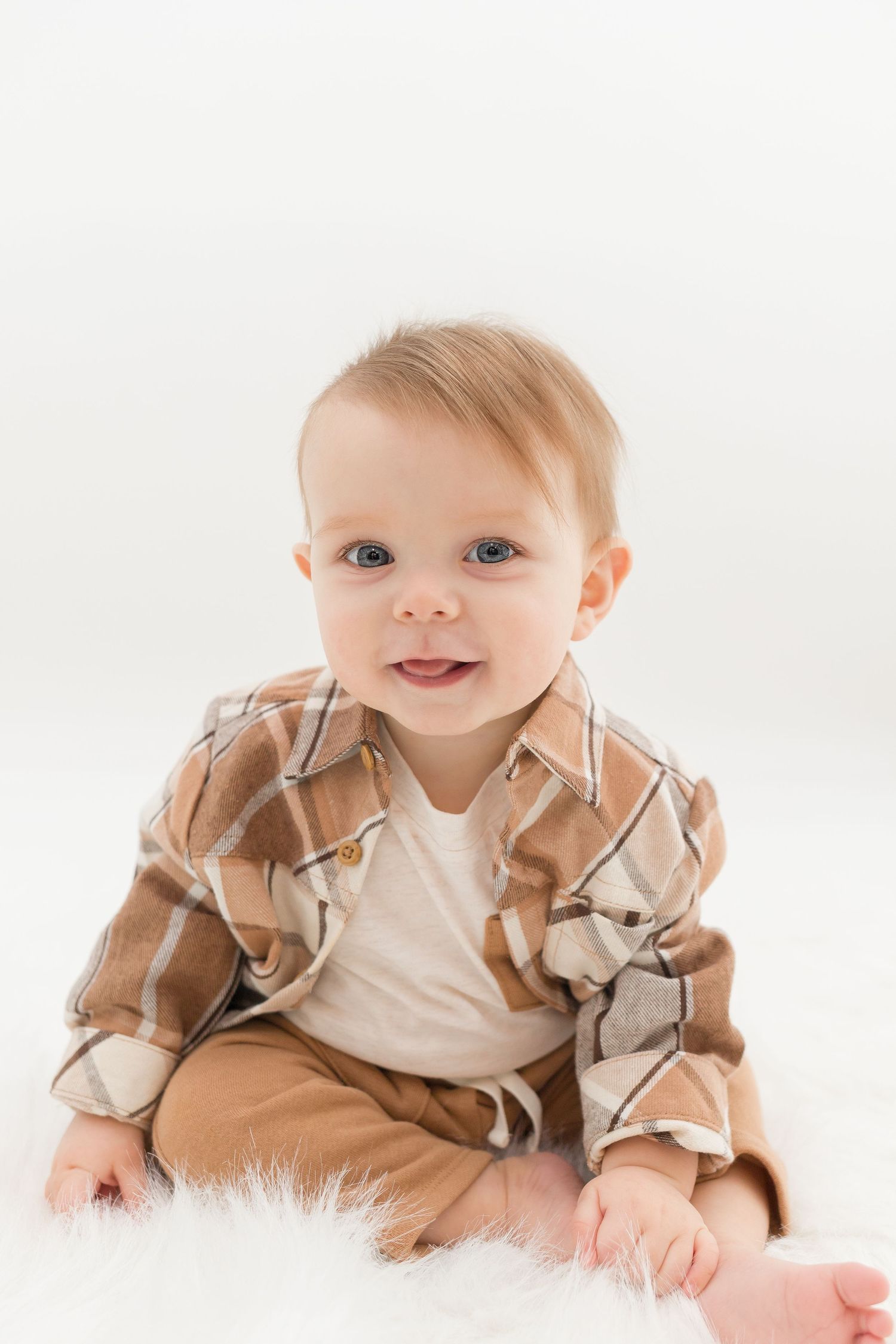 Baby wearing tan ruffled outfit lies on white fluffy rug.