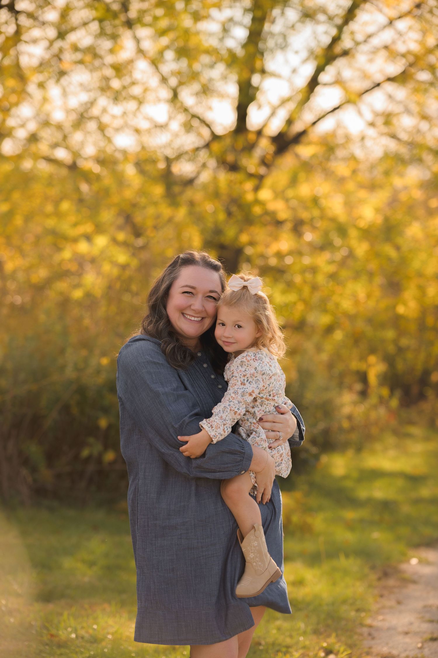 Parent holding small child against backdrop of golden autumn trees.