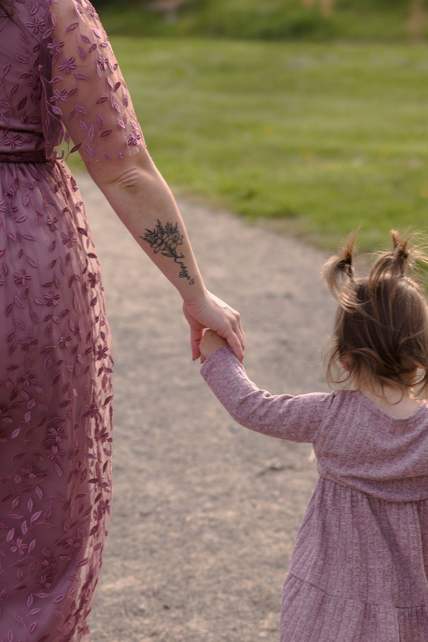 Close-up of a floral mauve dress and small hand holding together on a dirt path.