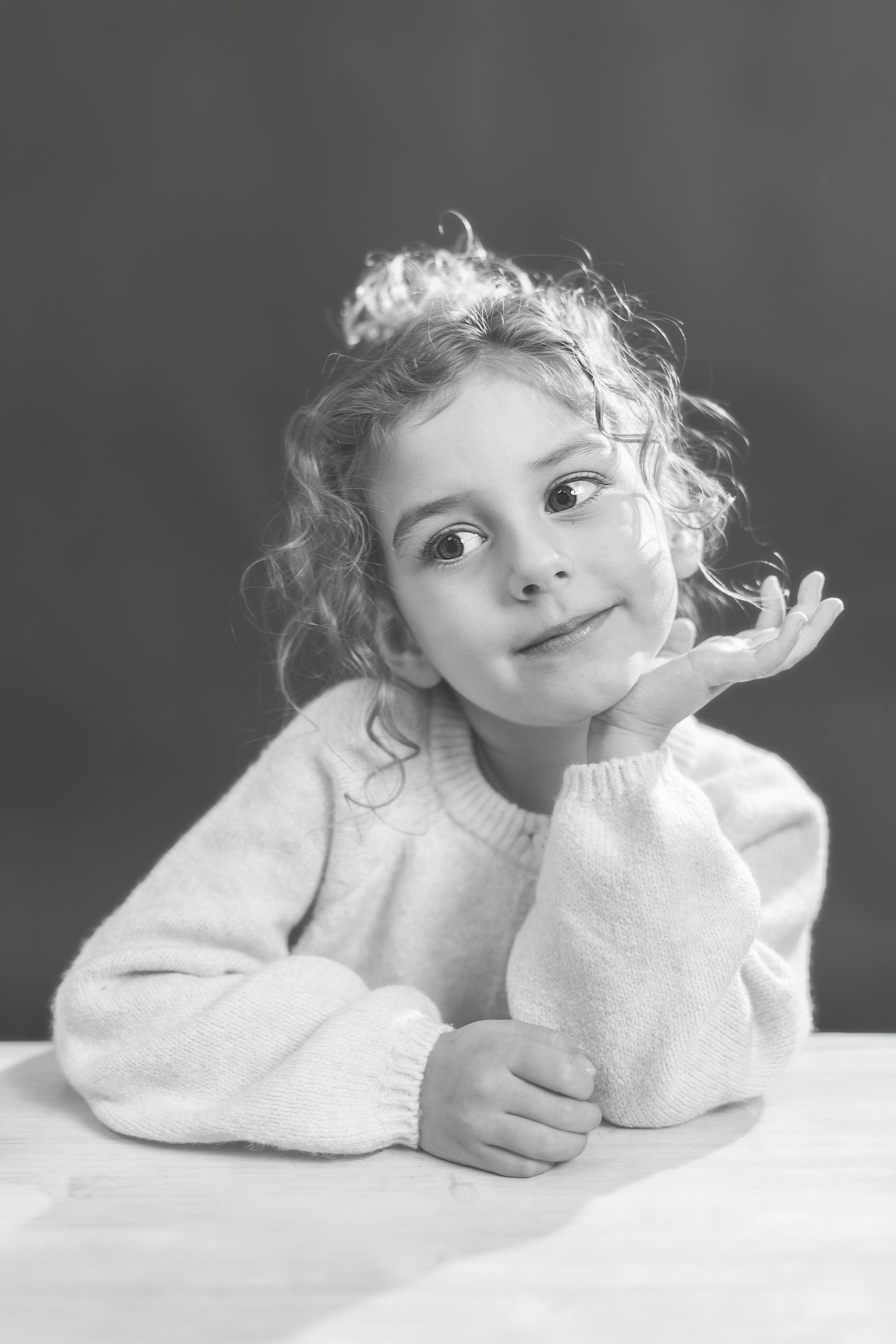A child in white lies on their stomach while playfully posing in a series of black and white portraits.