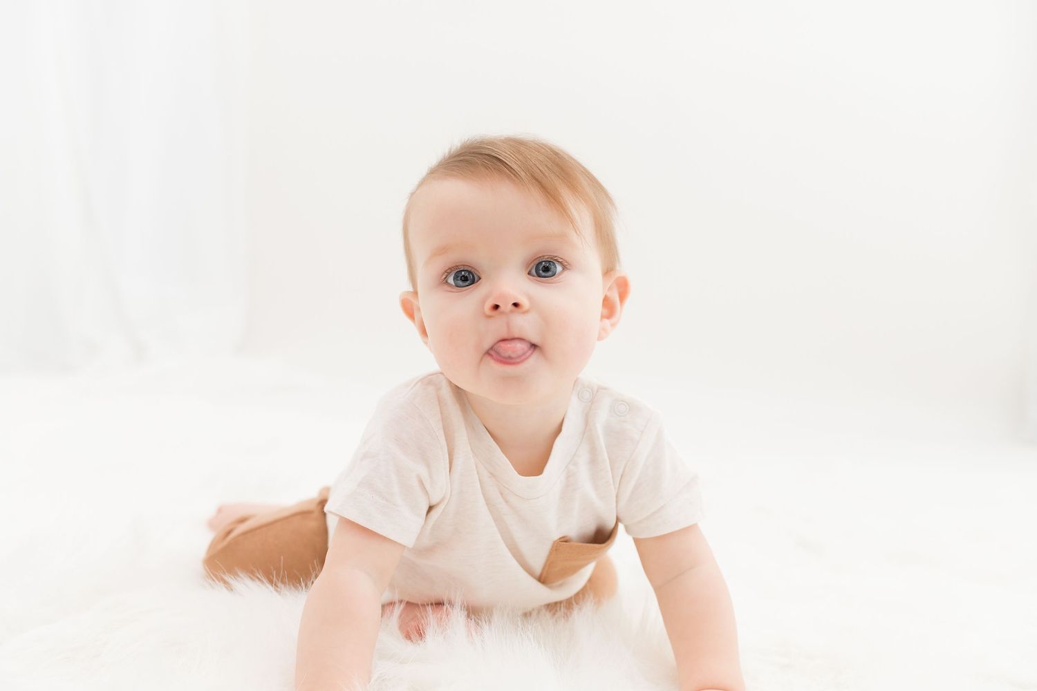 Baby wearing white onesie lying on soft white blanket in minimalist studio setting.