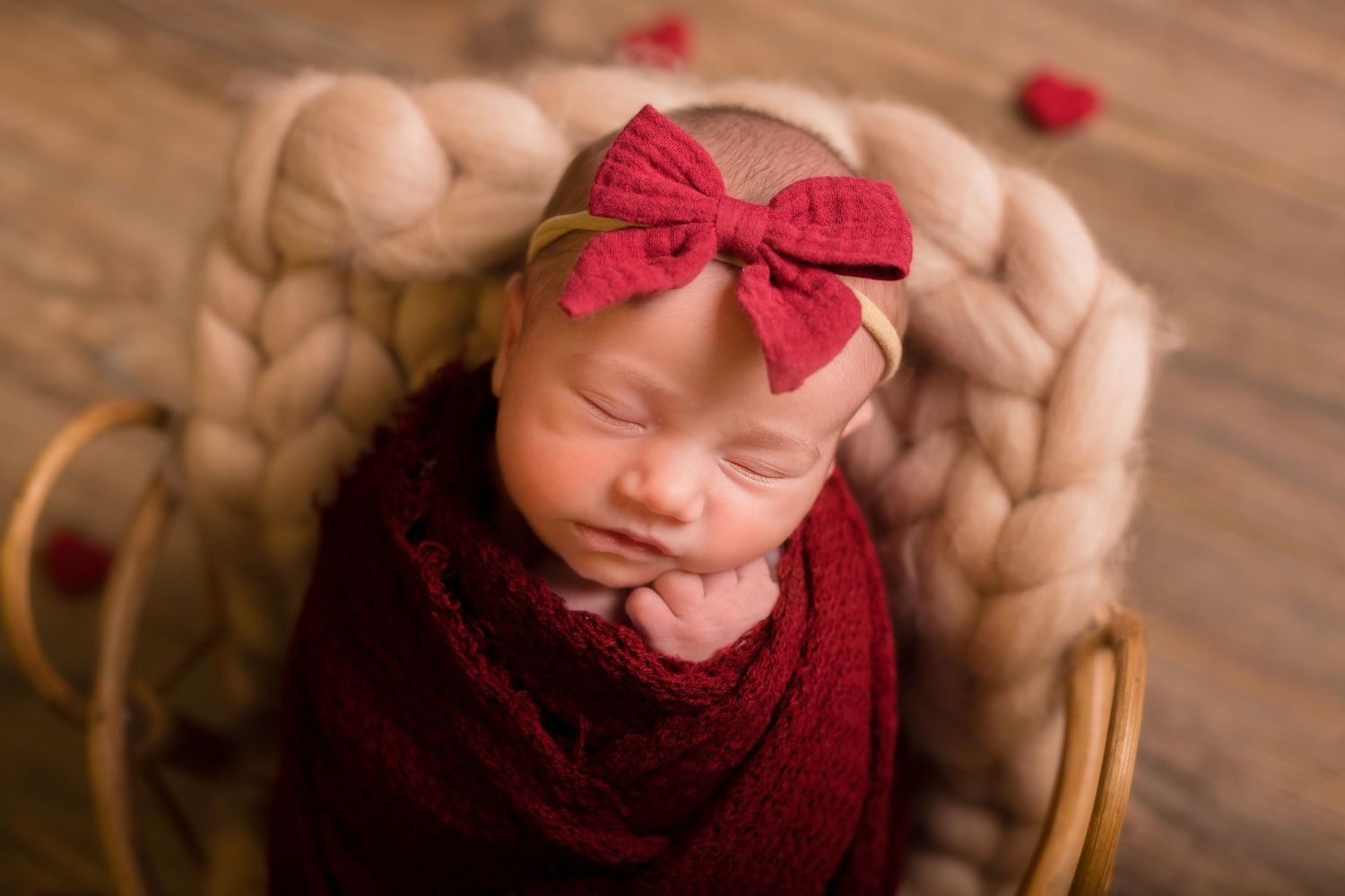 Artistic newborn portrait with burgundy wrap and rose petals on dark wood background.