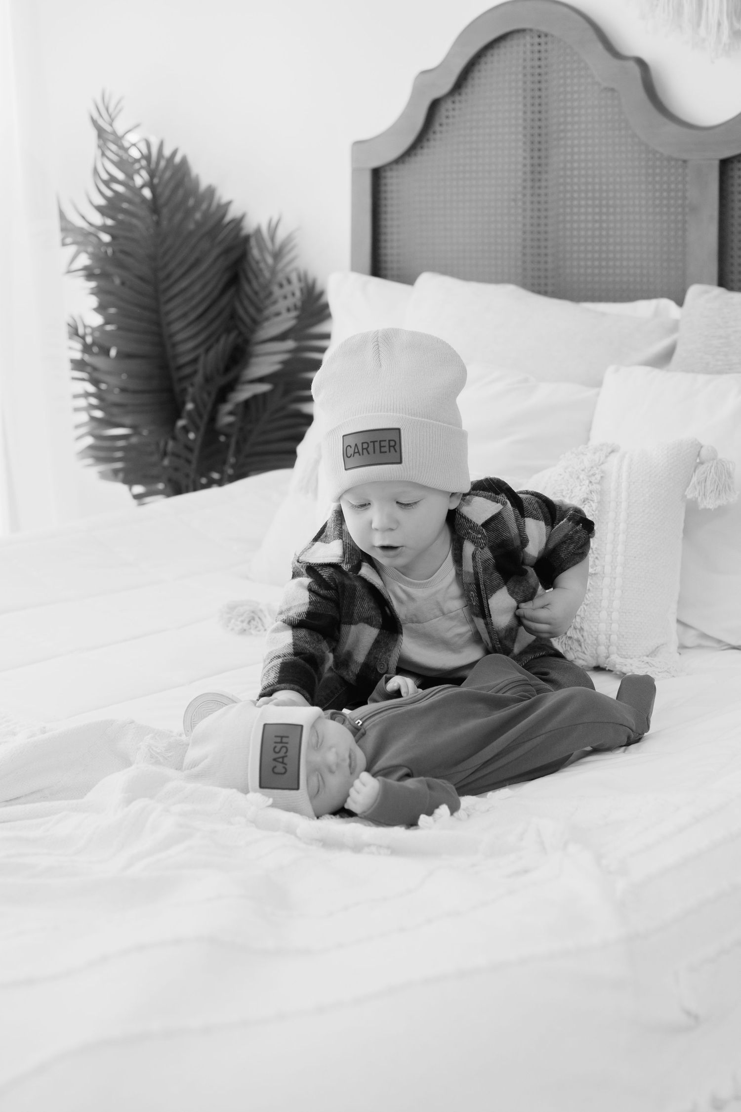 Black and white photo of small child lying on white bedding wearing winter hat.