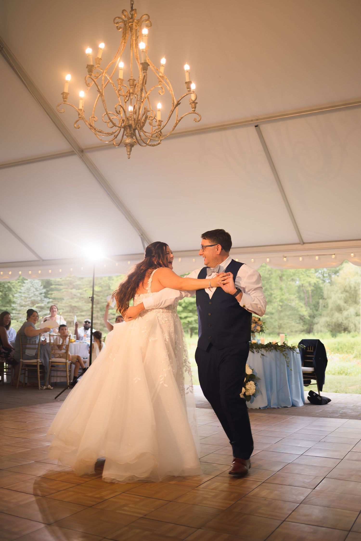 First dance under elegant chandelier in white wedding tent reception.